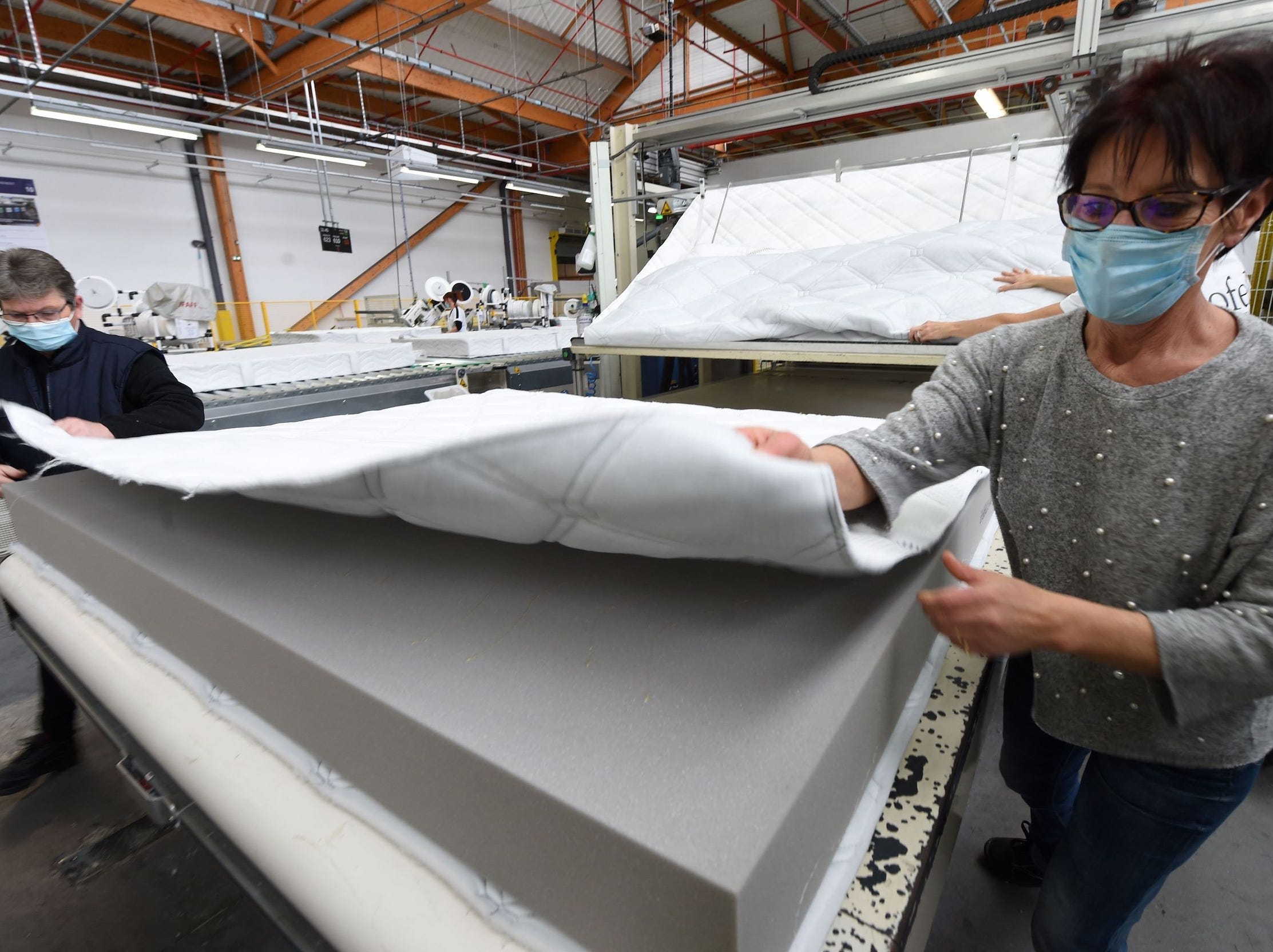 Two people wearing masks place cover on foam bedspring at mattress factory