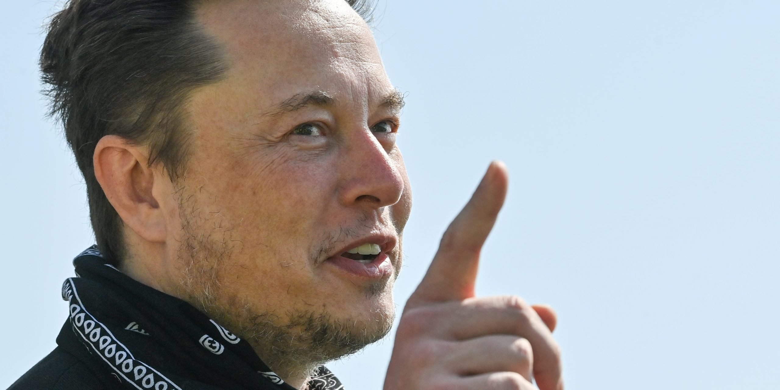 Tesla CEO Elon Musk points a finger upward while wearing a black bandana around his neck