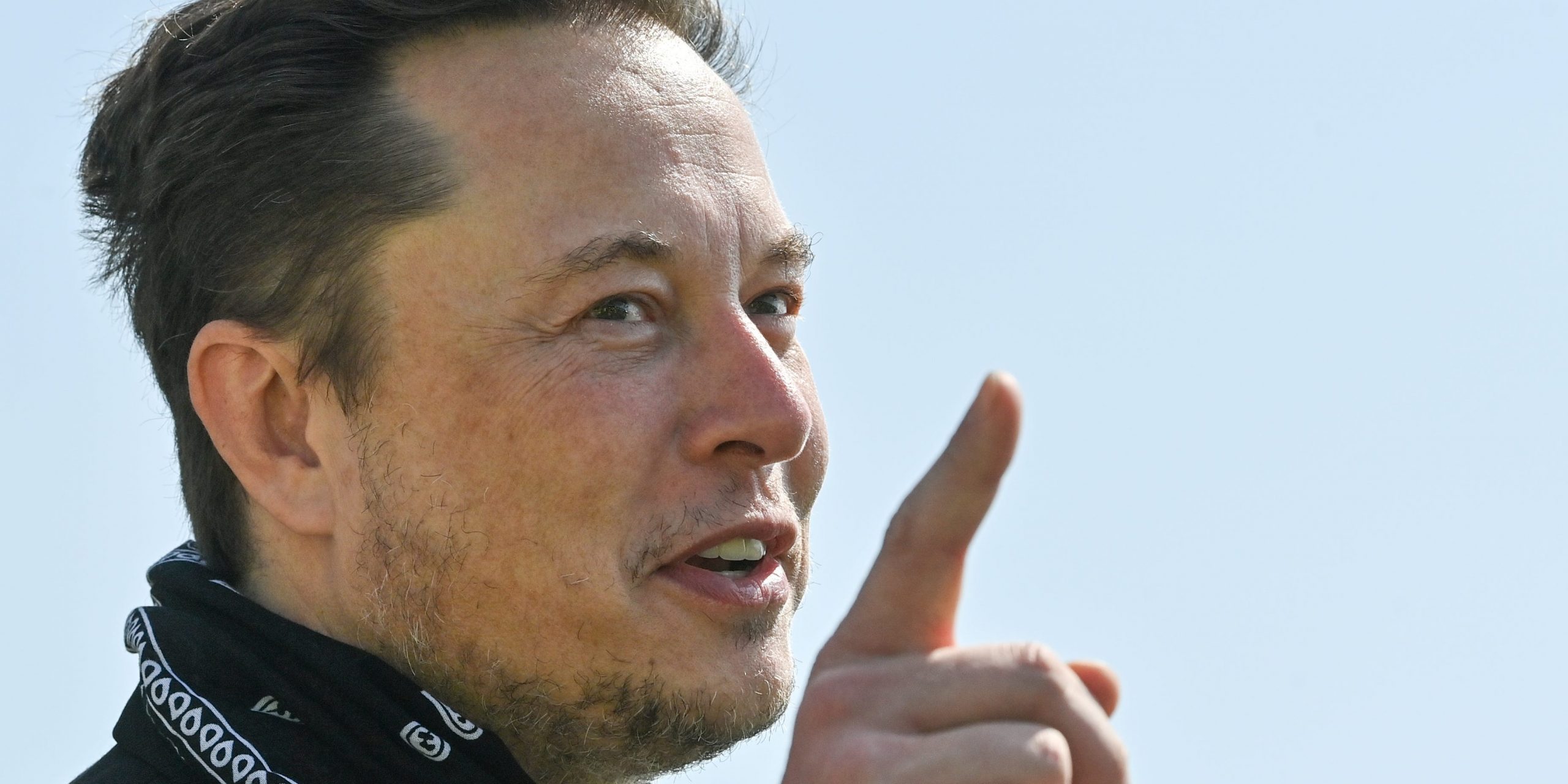 Tesla CEO Elon Musk points a finger upward while wearing a black bandana around his neck