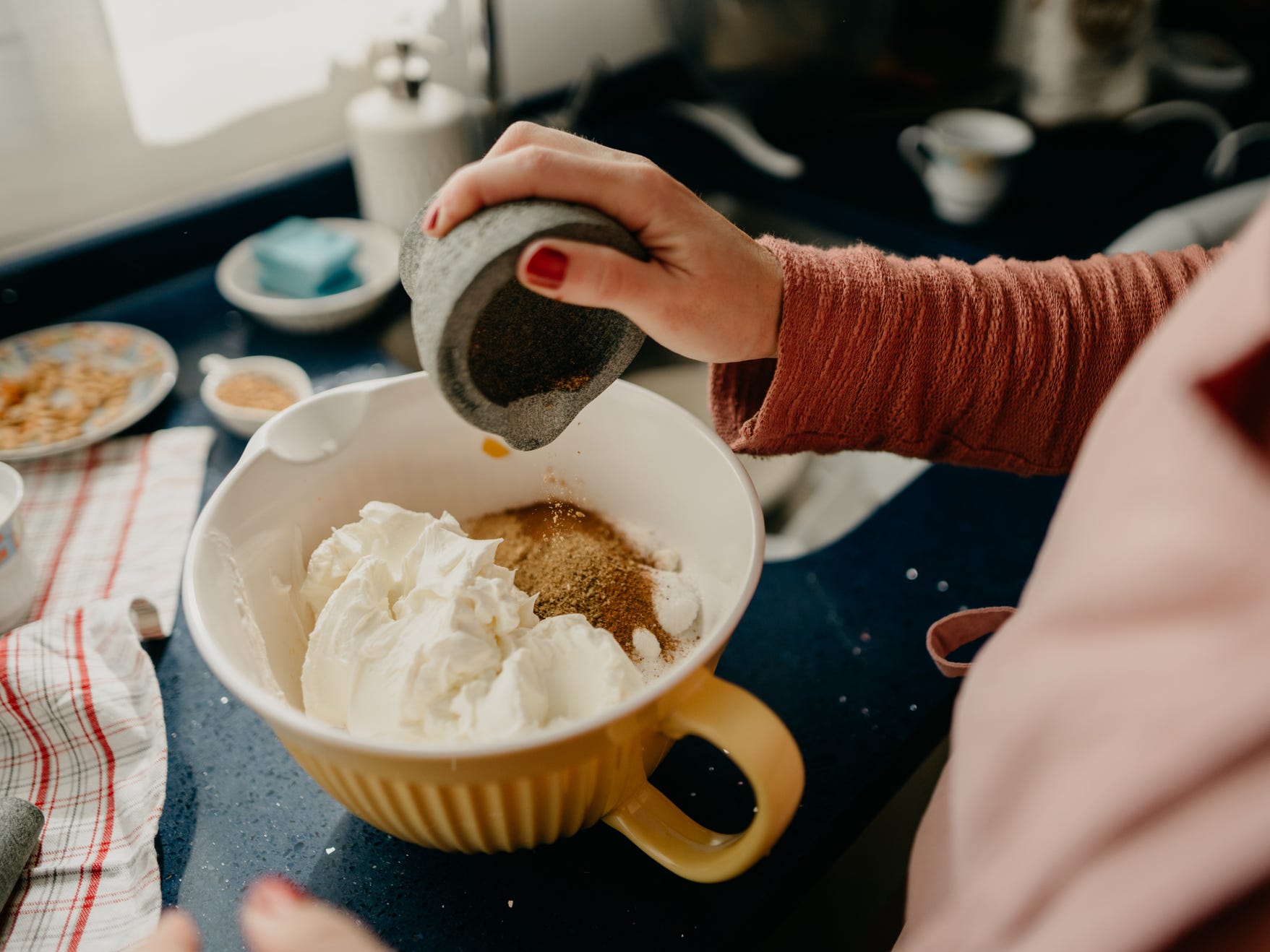 A home cook pouring a blend of spices into a bowl of ingredients