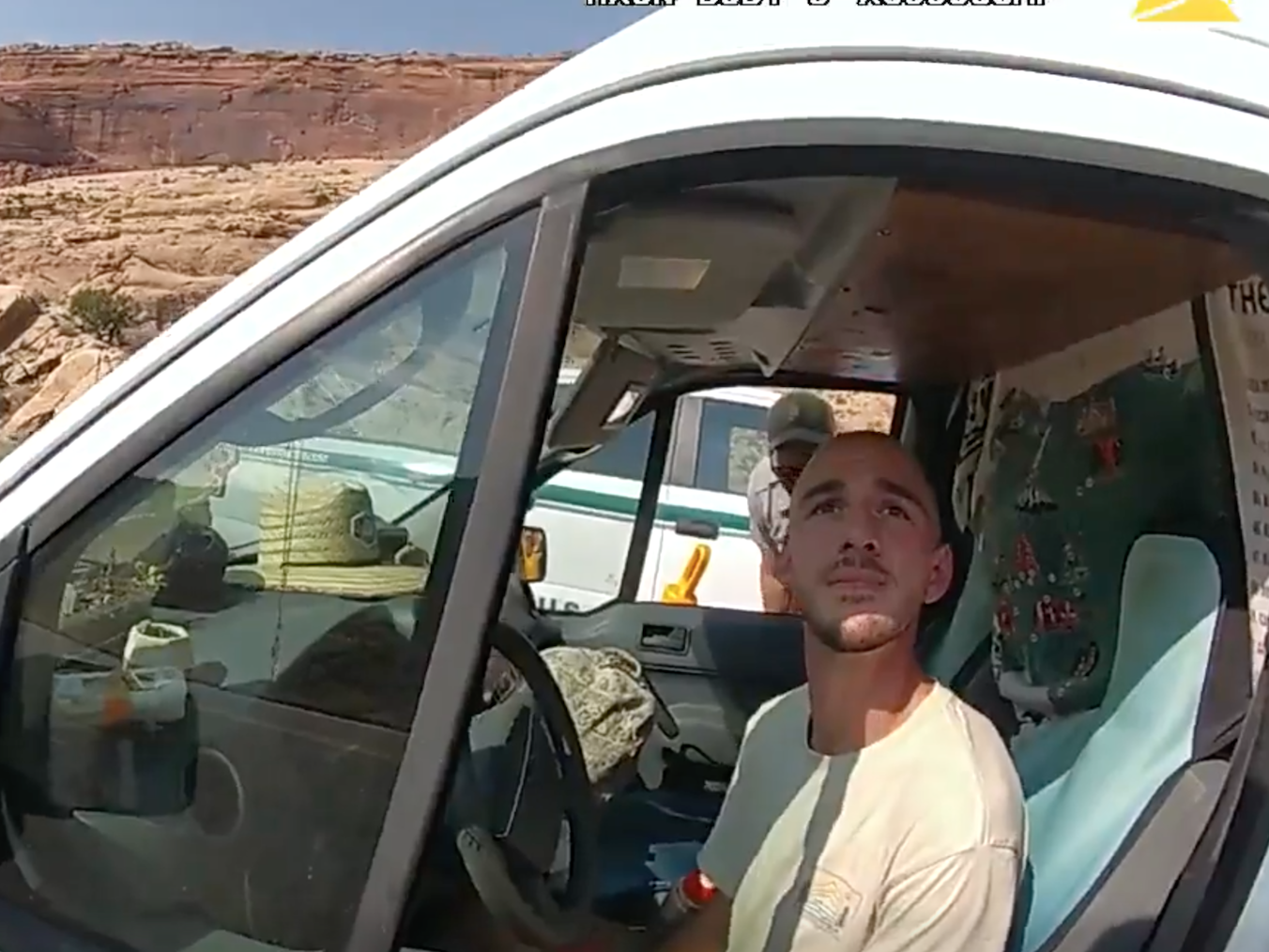 A Utah police officer's bodycam view of Brian Laundrie in the drivers' seat of a van. Laundrie is looking up at the officer.