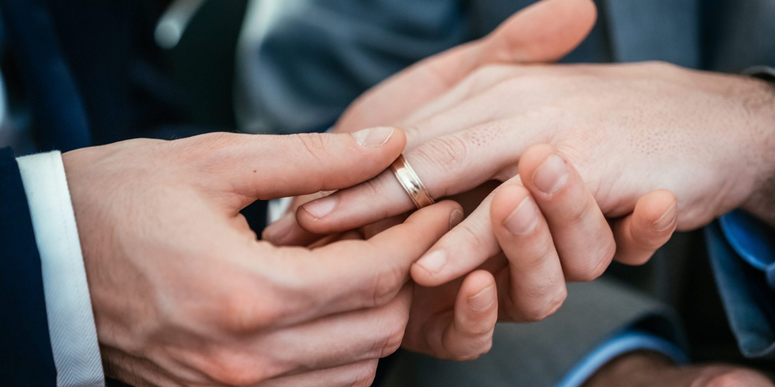 A man puts a wedding ring on another man's hand.