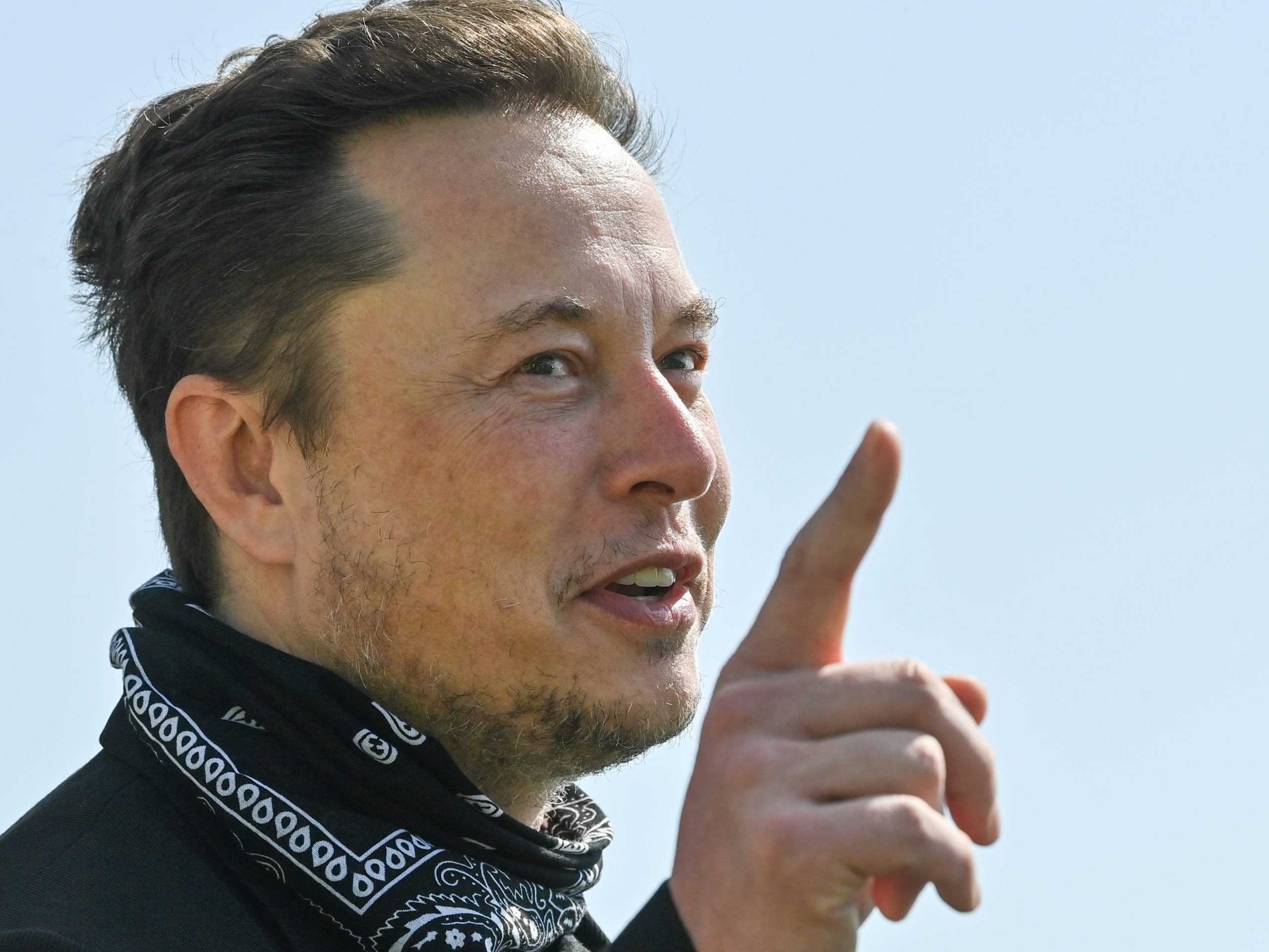 Tesla CEO Elon Musk points a finger upward while wearing a black bandana around his neck