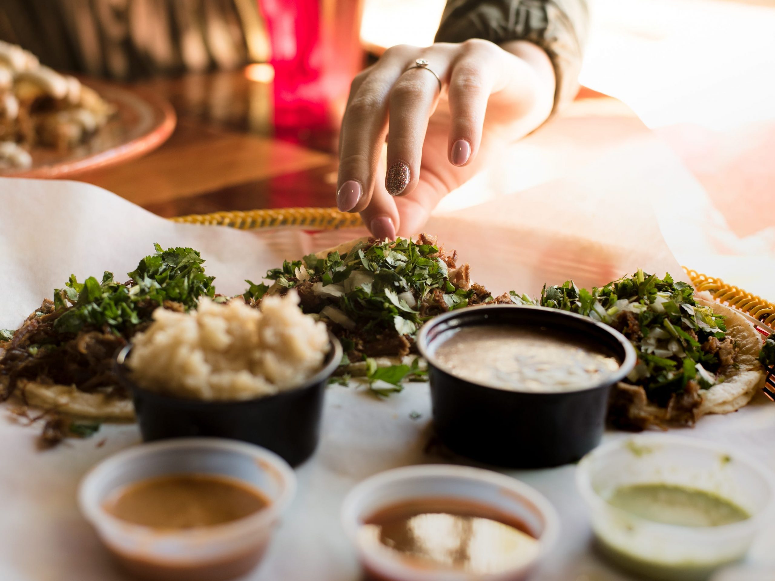 a plate of three tacos with a hand grabbing for one