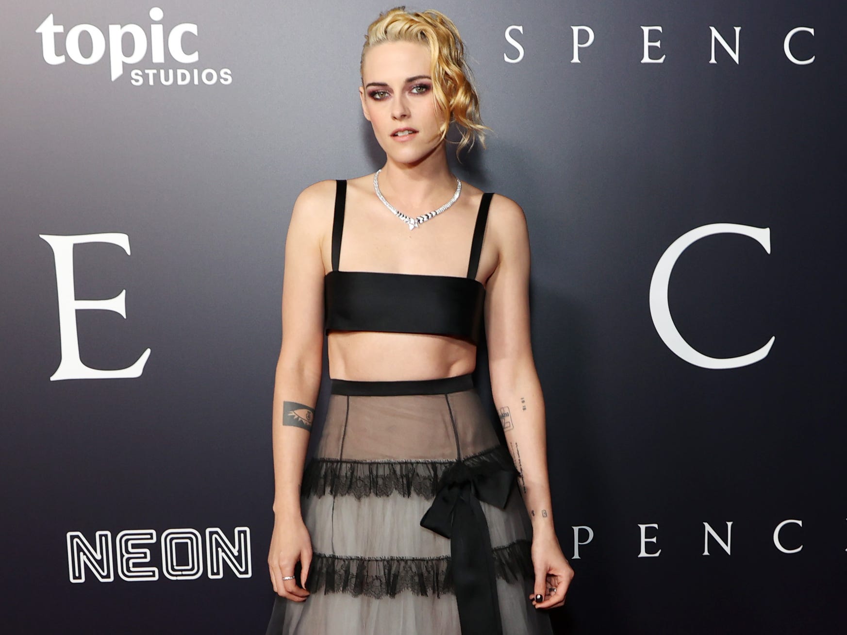 Kristen Stewart stands on a red carpet at the 'Spencer' premiere in a black and grey two-piece.