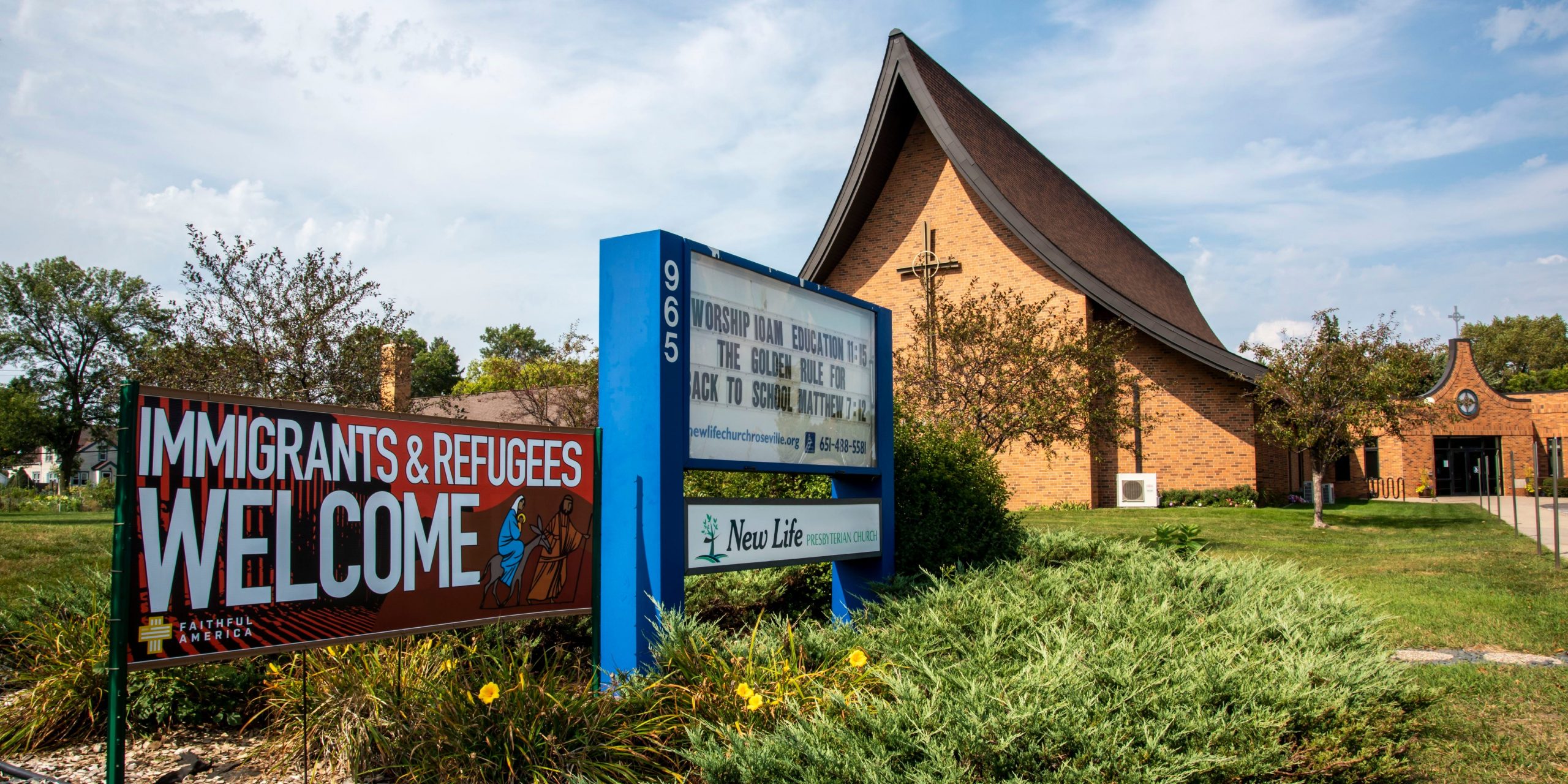 A banner in front of a church says "Immigrants & Refugees Welcome."
