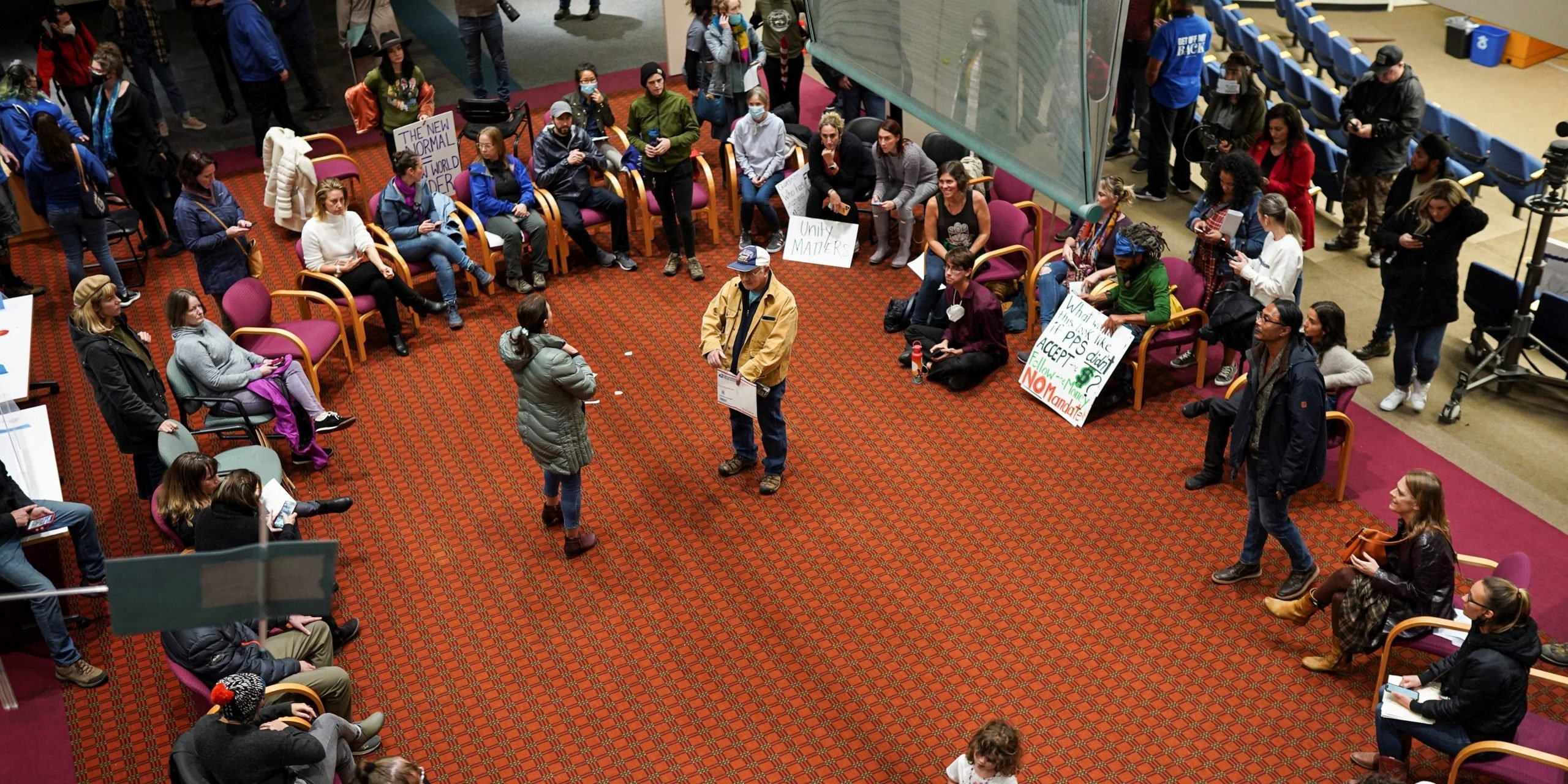 Demonstrators sit in a circle of chairs in the Portland School Board building's lobby.