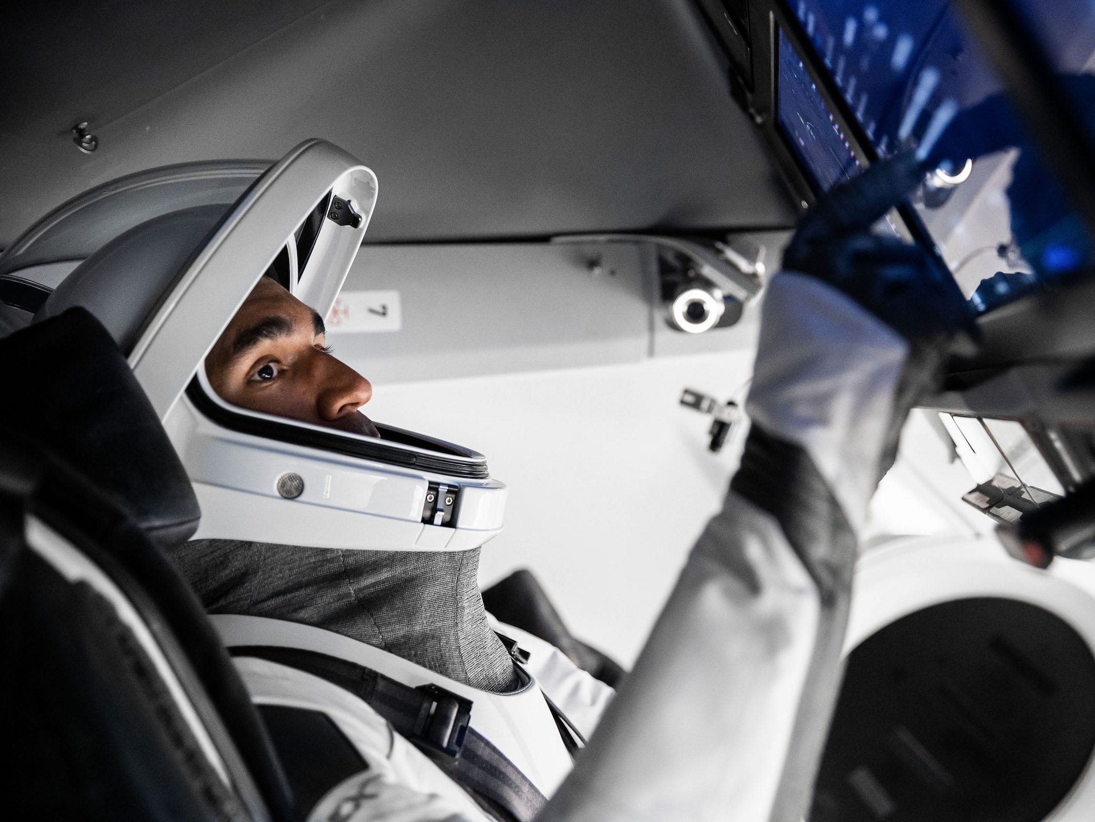 astronaut Raja Chari in white grey spacex spacesuit inside spaceship operating touchscreen controls