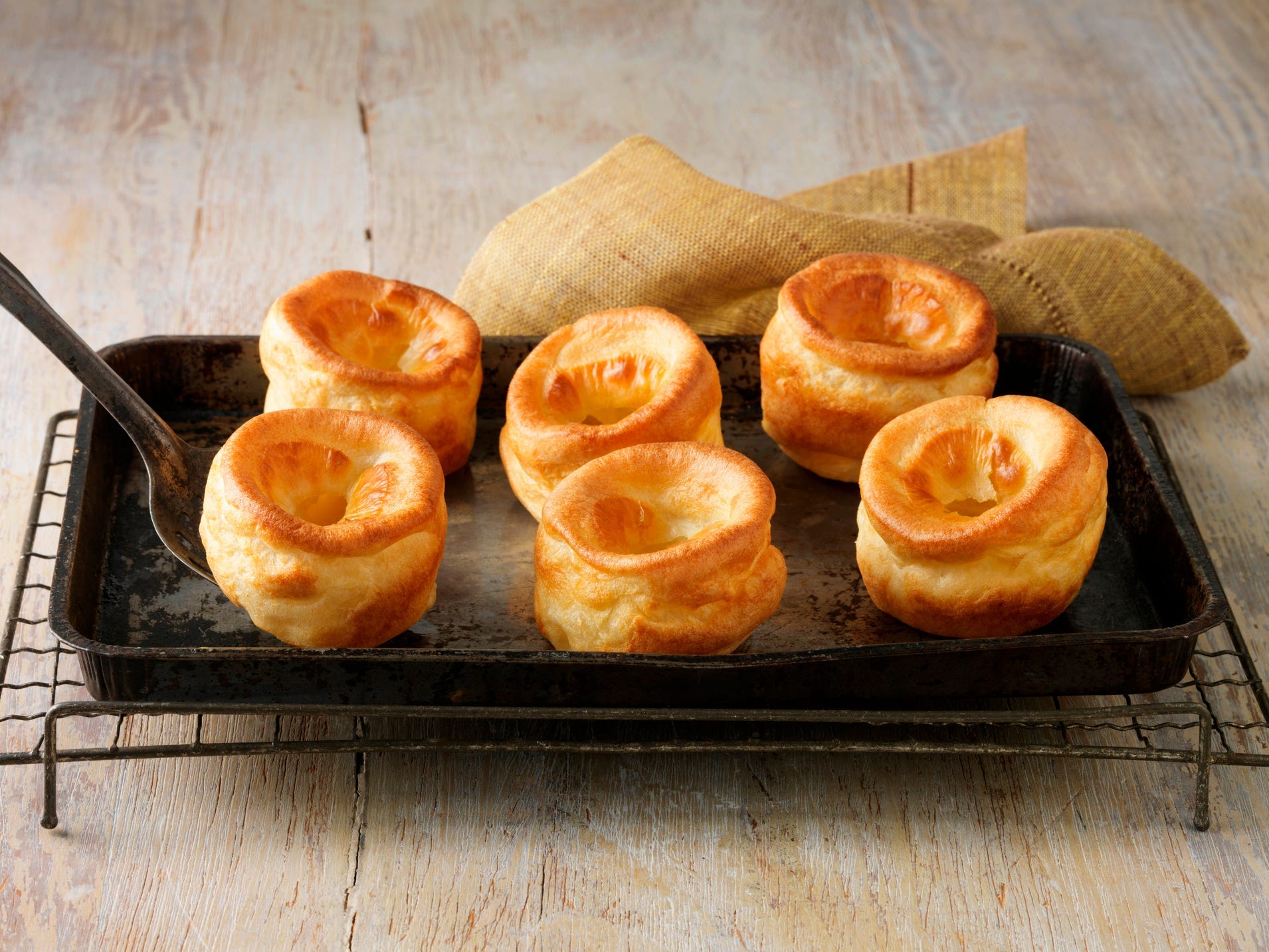 Six Yorkshire puddings on a metal tray.