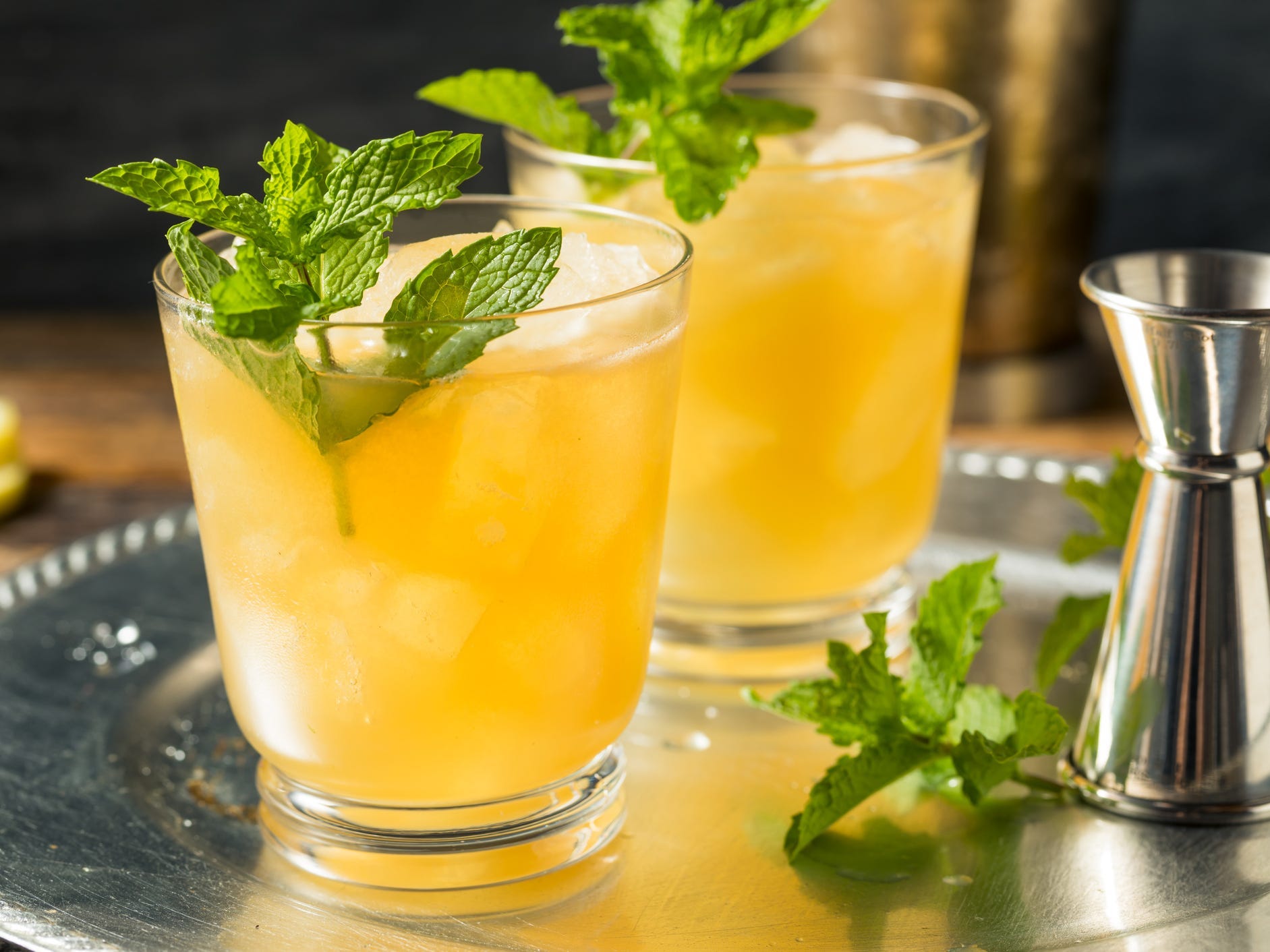 Two whiskey smash cocktails on a silver tray garnished with mint