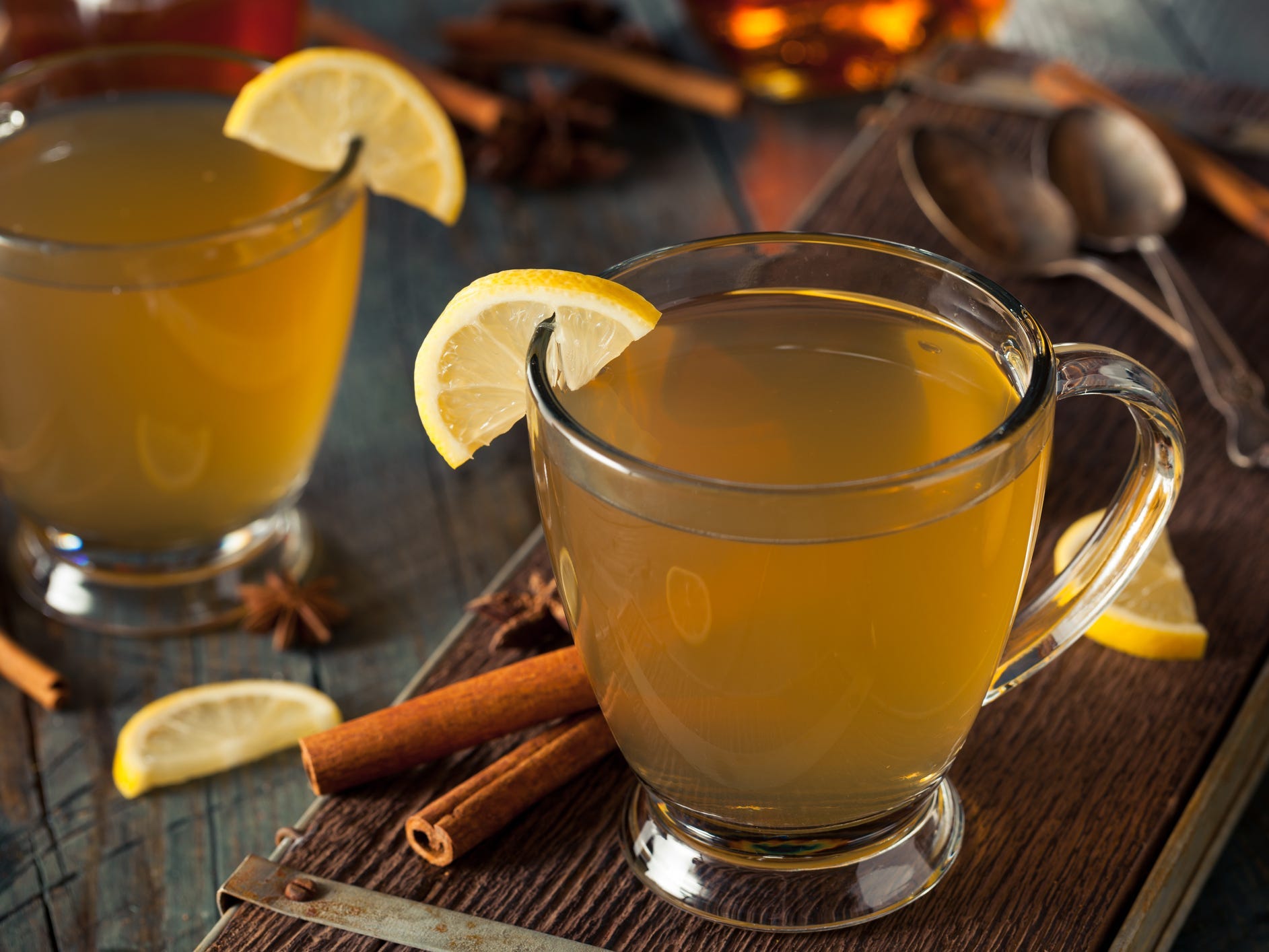 A hot toddy in a clear glass mug garnished with a lemon slice