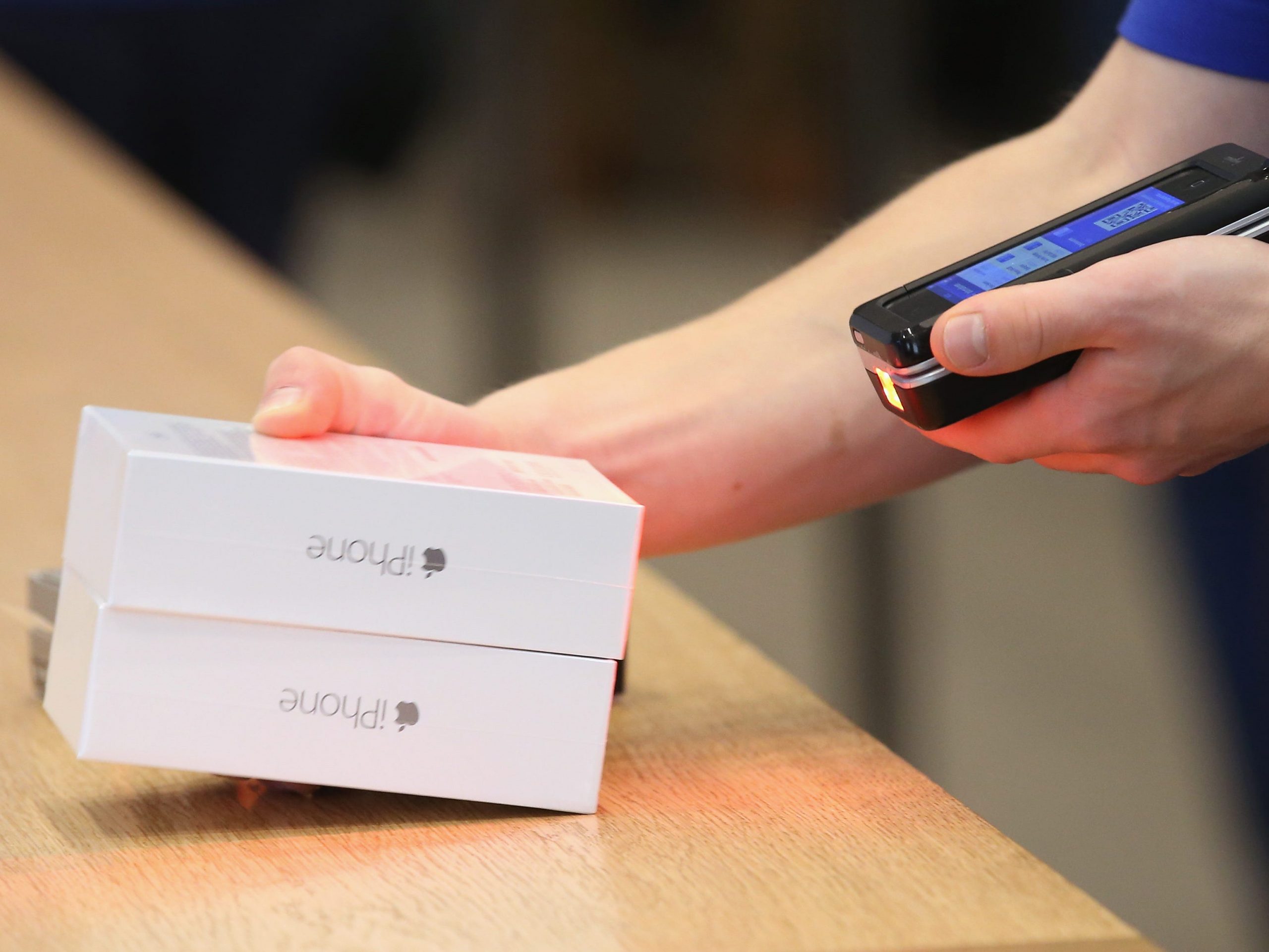 Close up of an Apple Store employee's hands holding two new iPhone boxes and scanning them with a special handheld sales device.