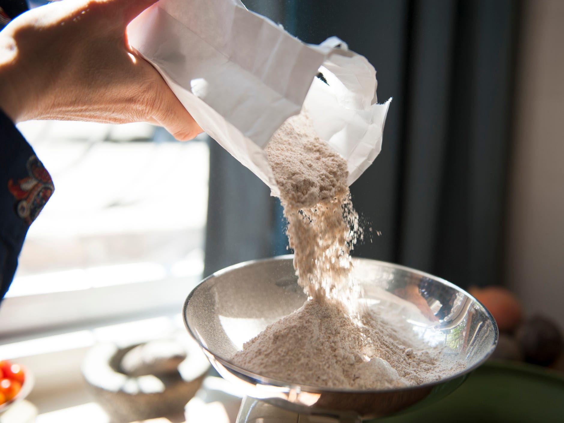 Someone pouring flour into the bowl of a scale.