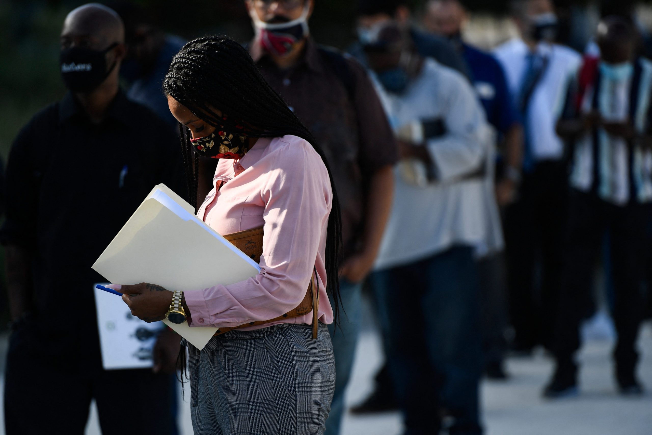 A woman in a pink shirt holds a folder in a line at a job fair in Los Angeles