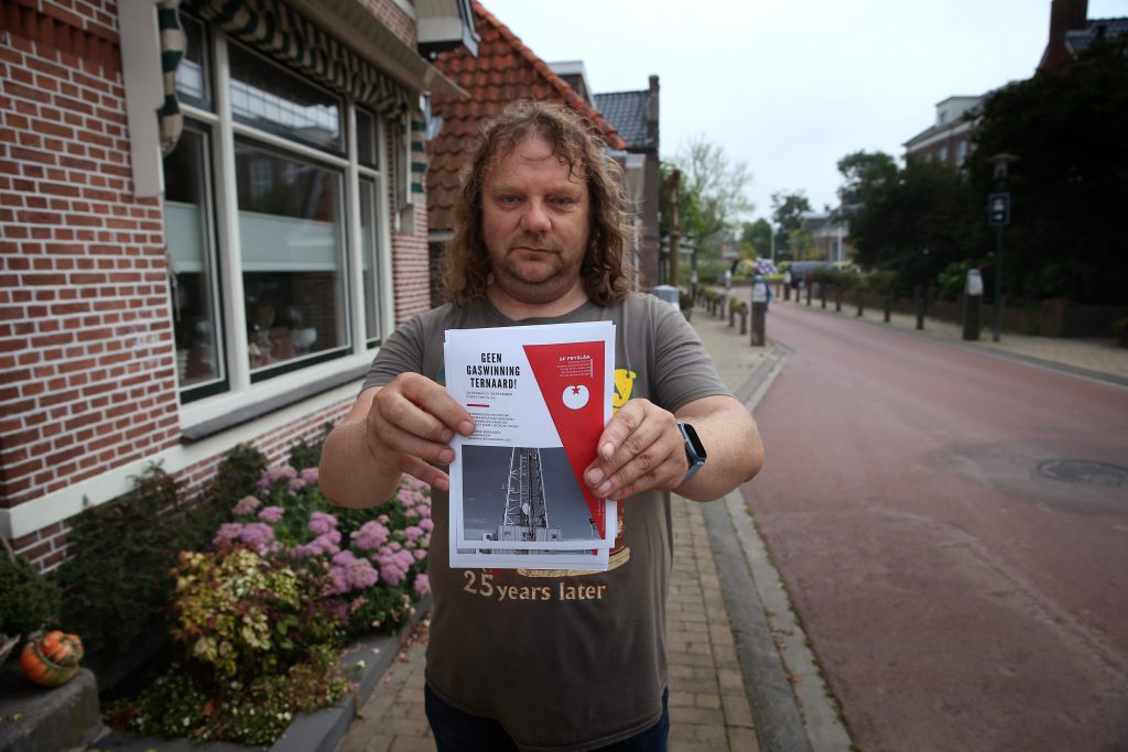 Een inwoner van het Friese dorp Ternaard houdt een pamflet vast waarop het protest tegen gaswinning wordt aangekondigd.
