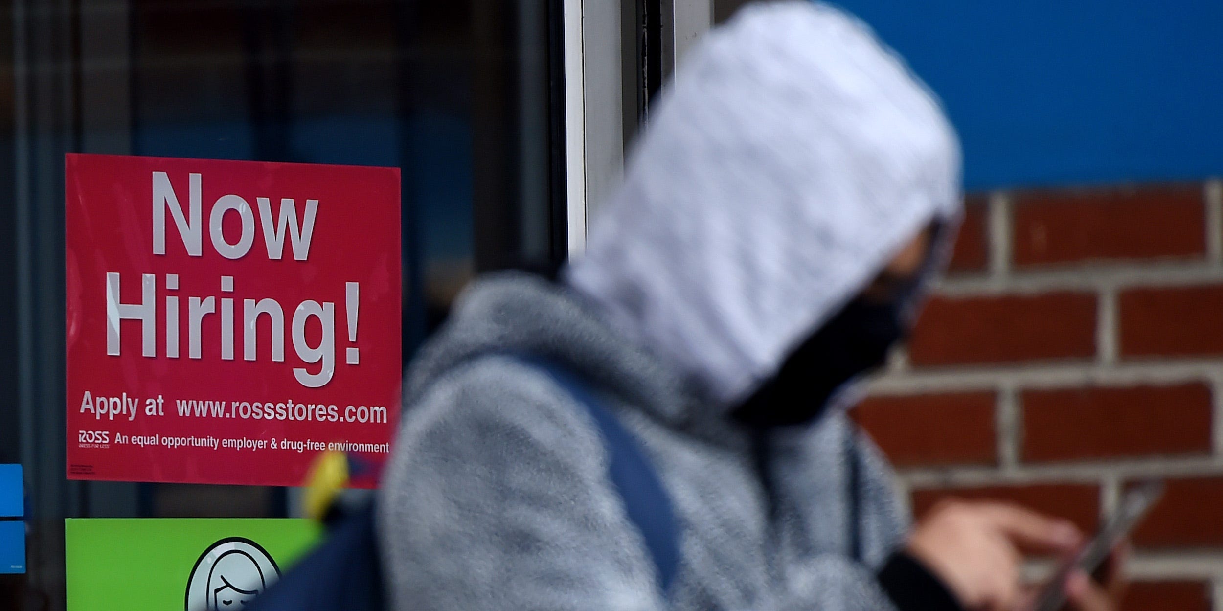 A person in front of a "Now Hiring!" sign.