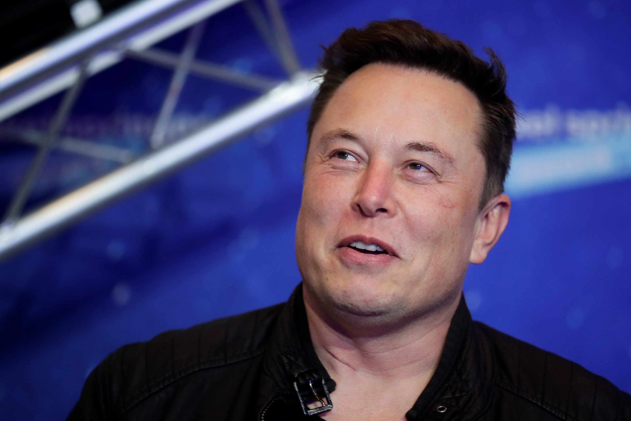 Tesla CEO Elon Musk smiles in front of a blue background