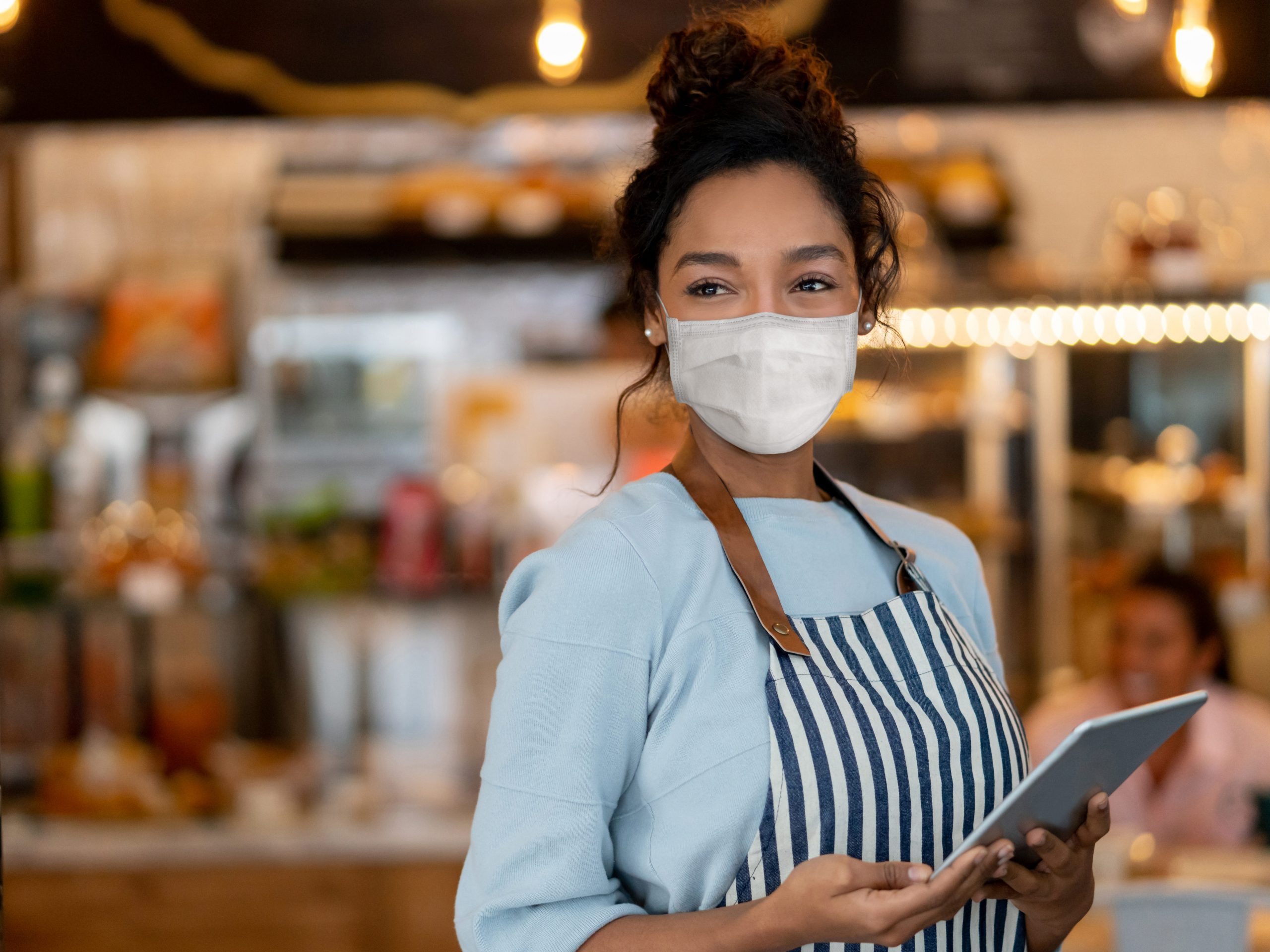 A restaurant worker wears a facemark while holding a tablet to take customer orders.