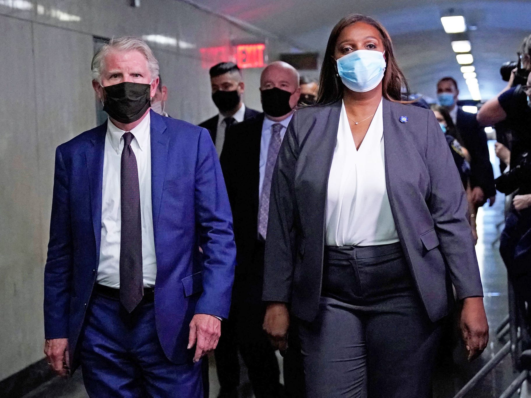 Cyrus Vance Jr. and Letitia James, wearing face masks, walk in a hallway followed by several other people.