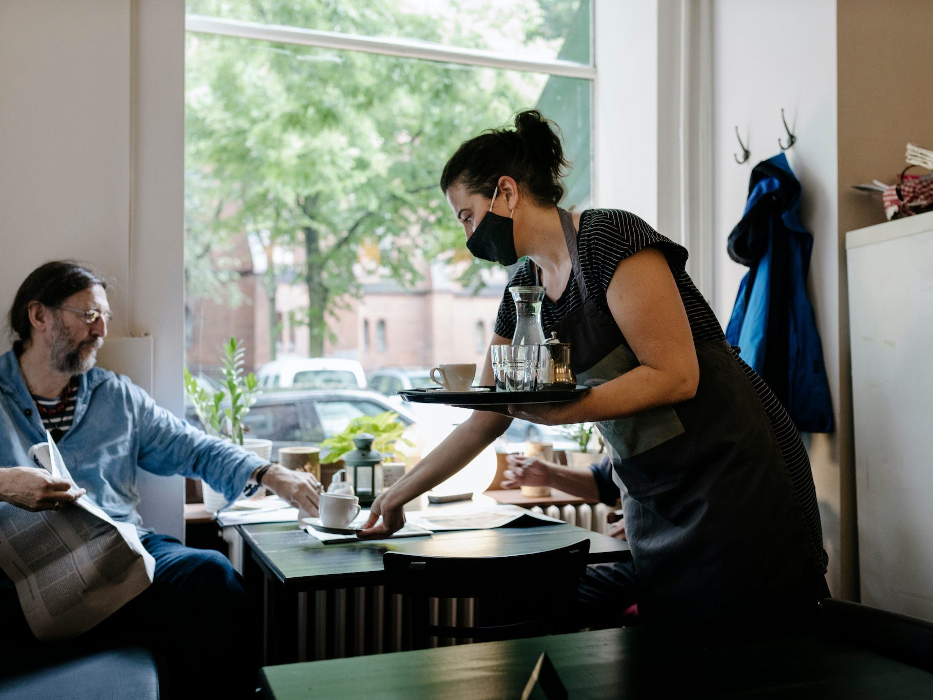 A waitress wearing a face mask and serving a customer some coffee at his table in a restaurant.