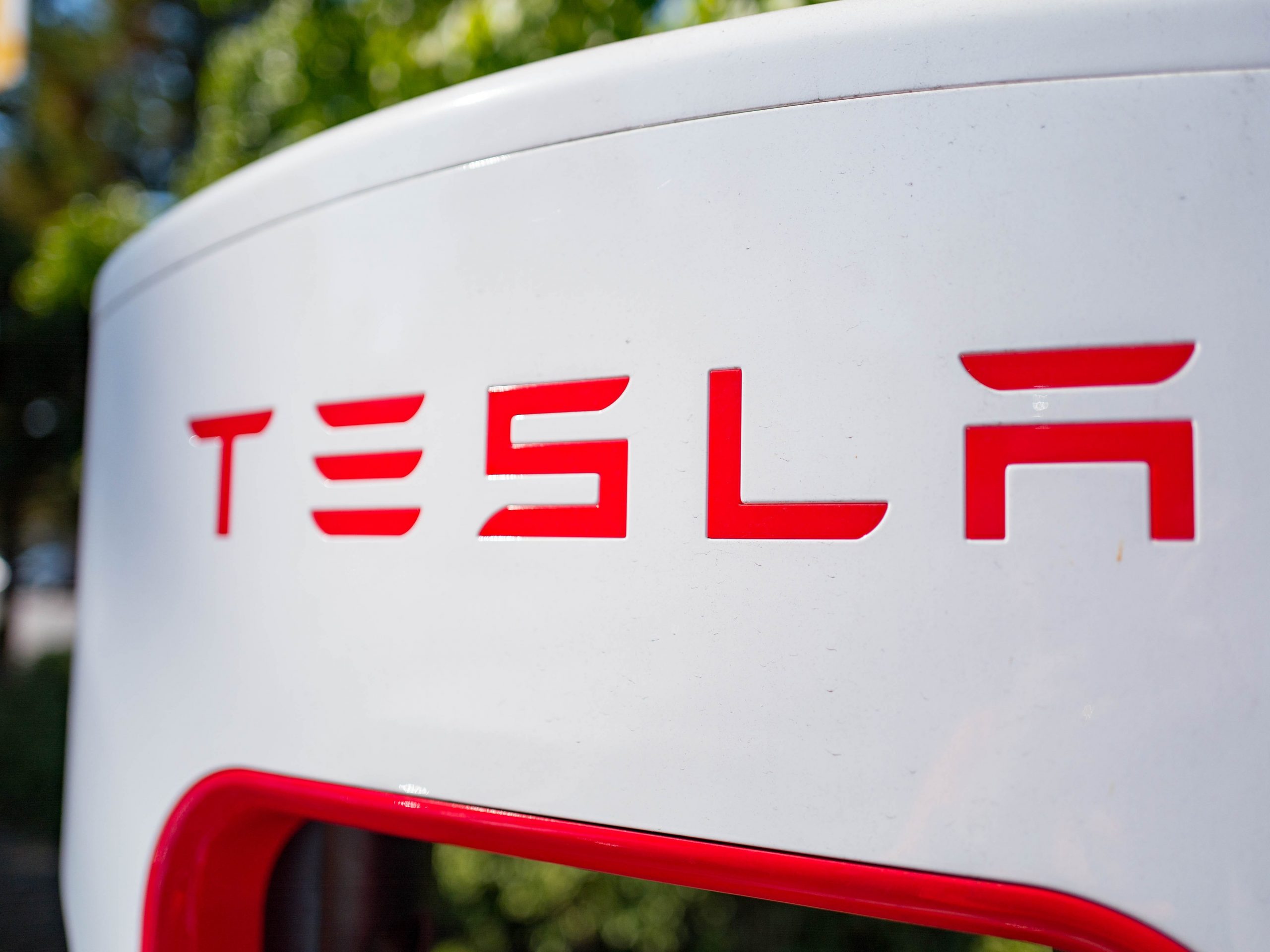 A close-up red Tesla logo on a white background.