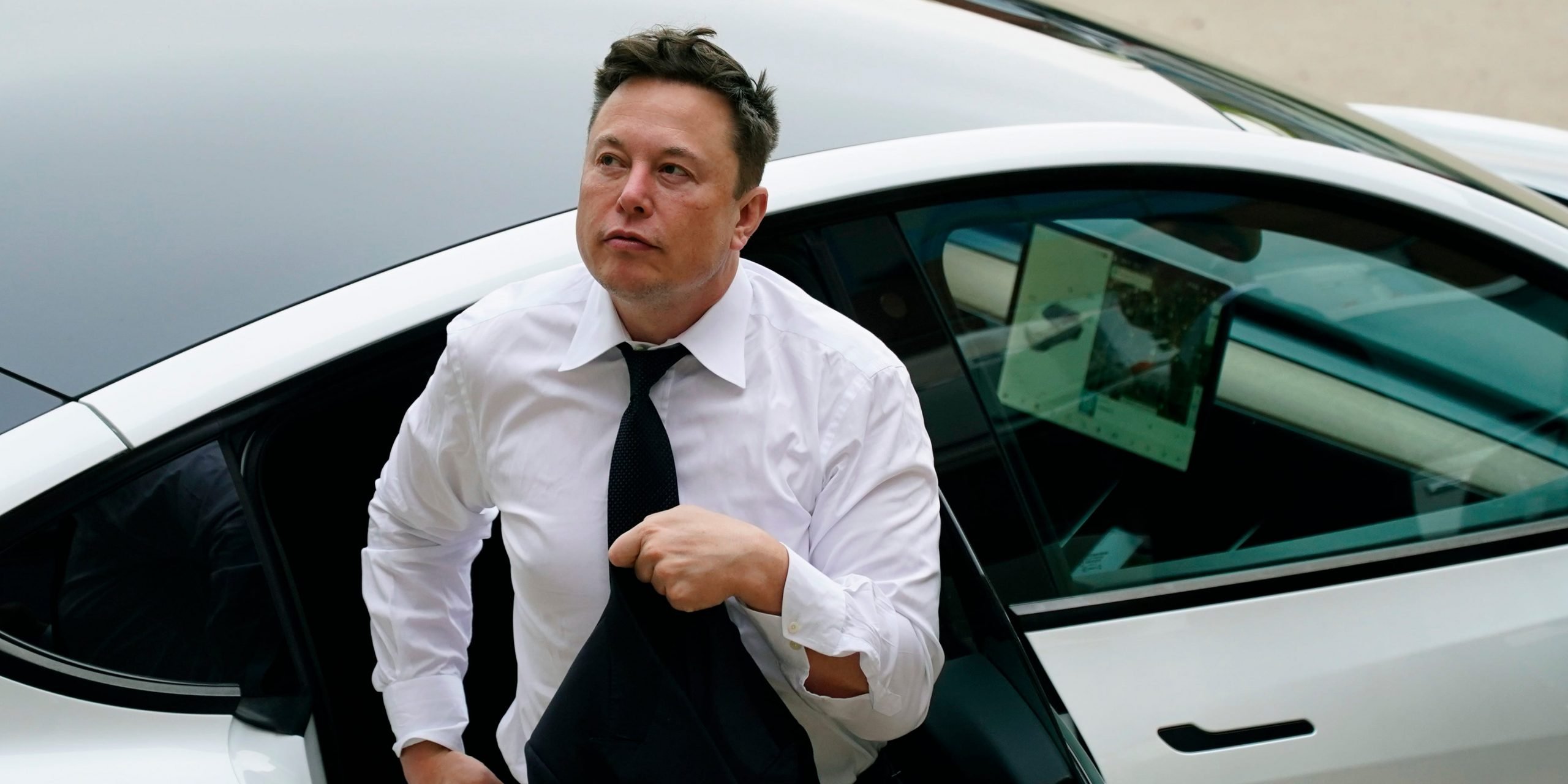 Tesla CEO Elon Musk in a white shirt and tie exits the backseat of a white Tesla