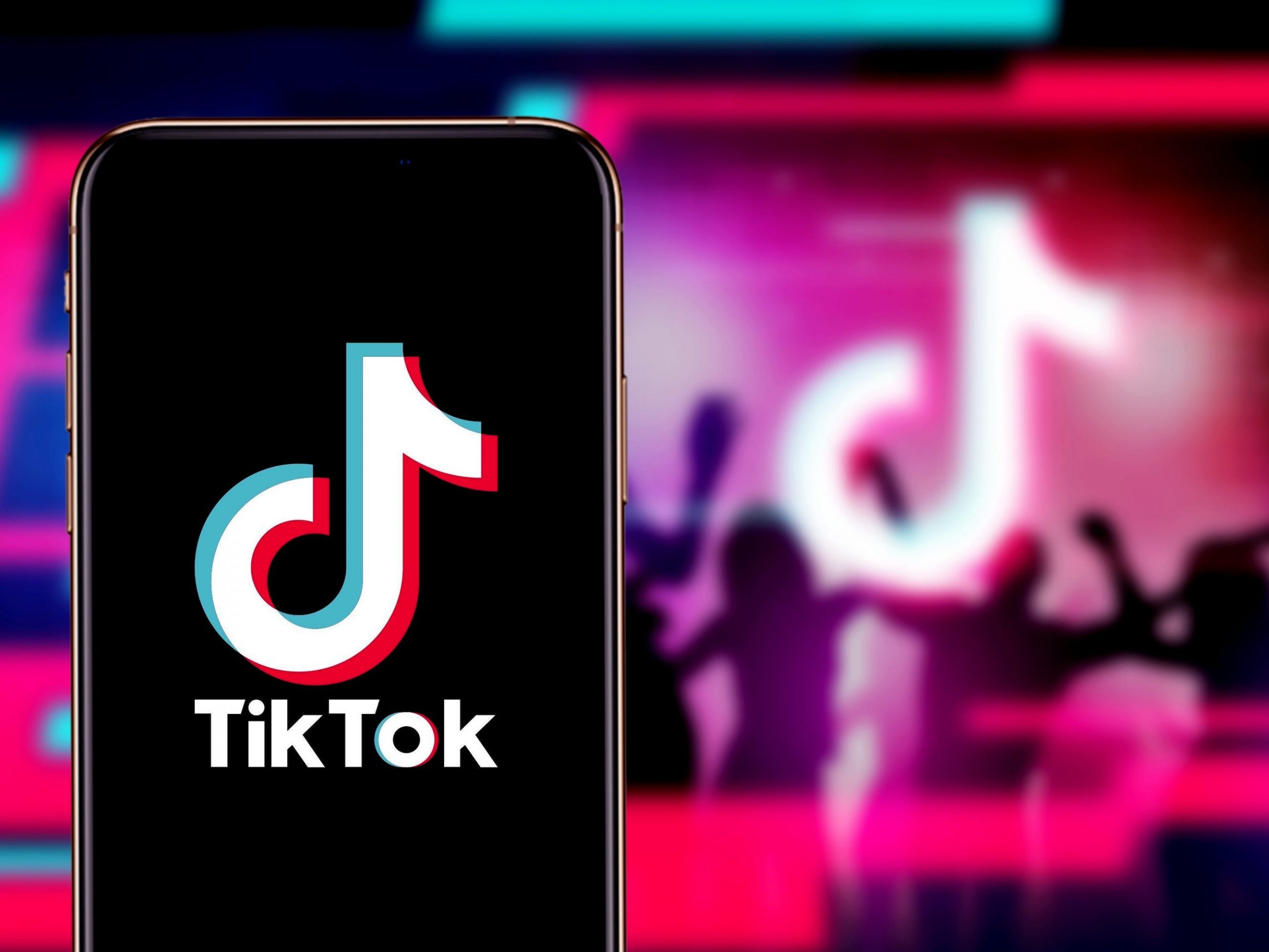 An iPhone displaying the TikTok logo. In the background, silhouettes dance around a TikTok logo.