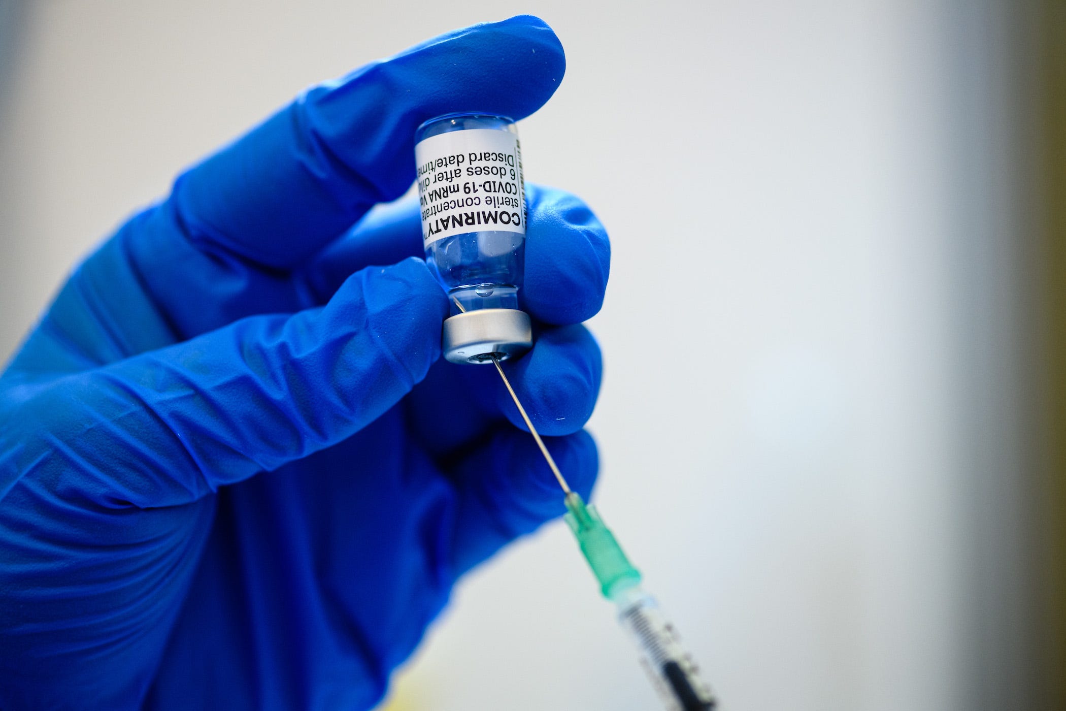 a healthcare worker holds a syringe inserted into a vial of pfizer's comirnaty vaccine