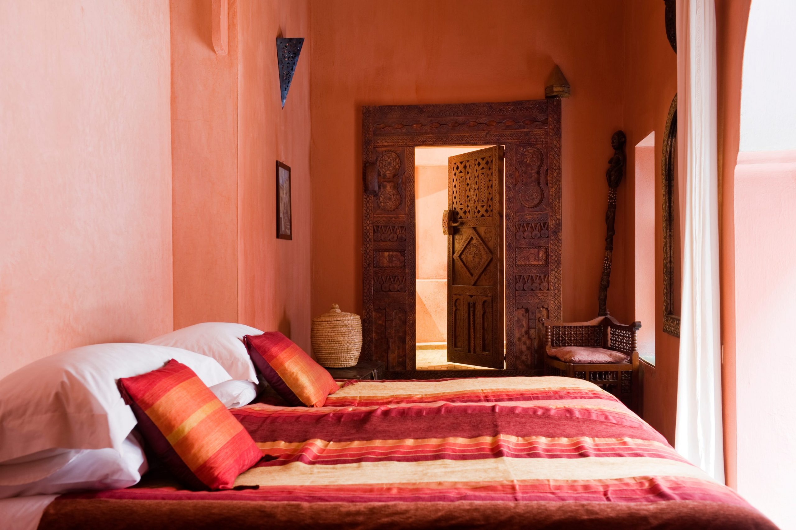 A sandy pink-painted bedroom with two beds adorned in pink, red, and orange linen.