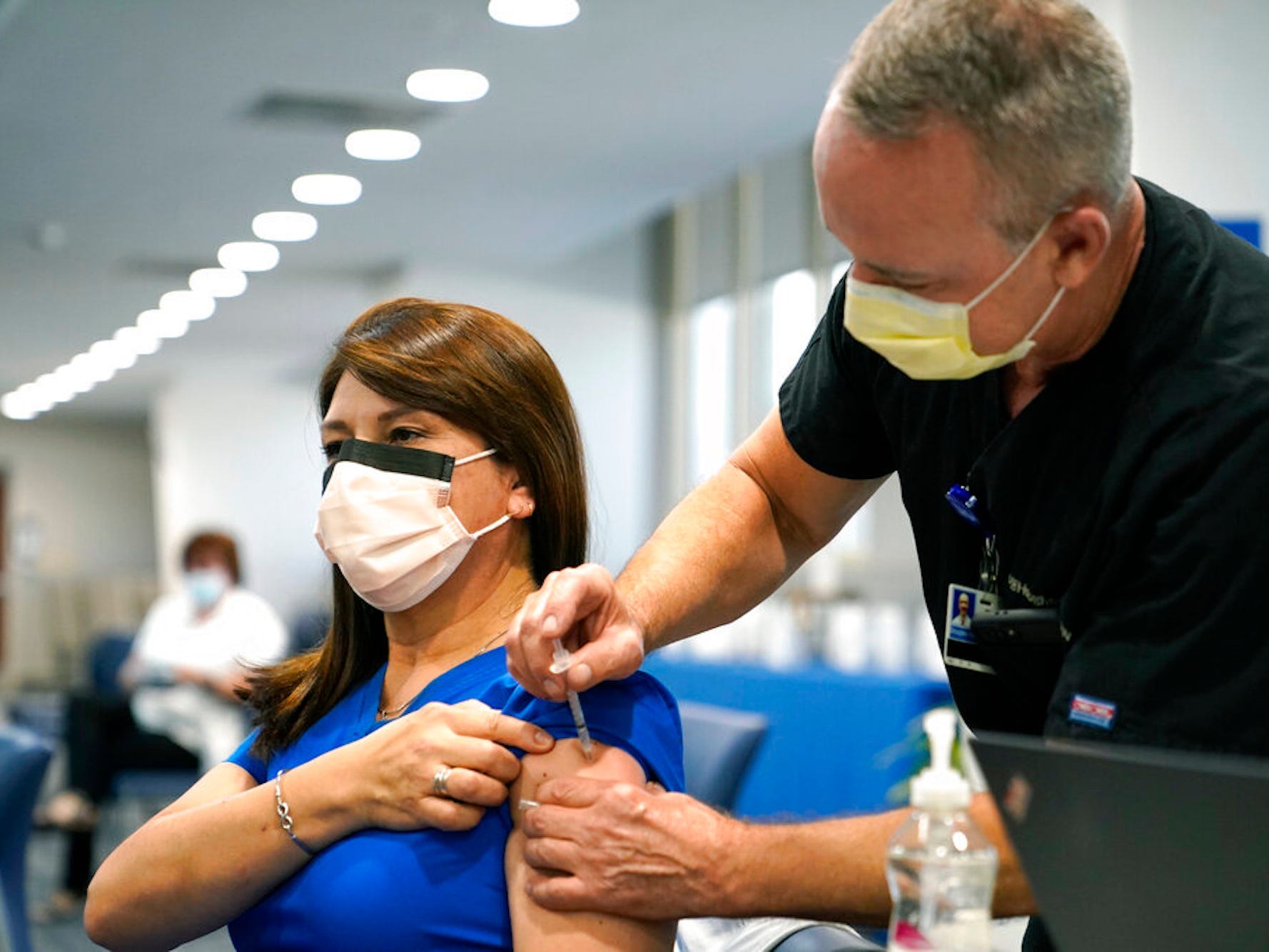 A woman wearing a mask and blue scrubs gets a shot in a clinic.