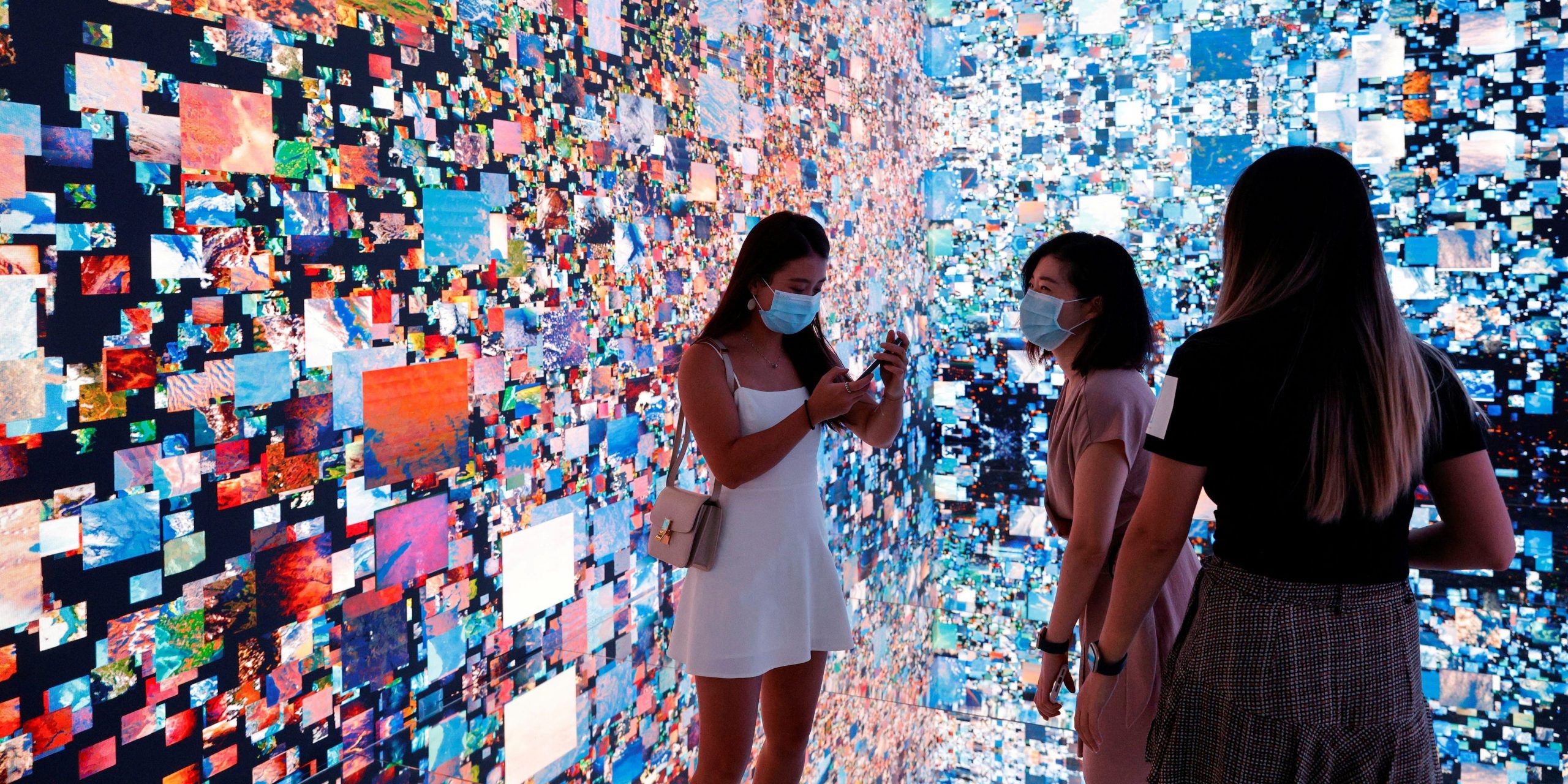 Visitors are pictured in front of an immersive art installation titled "Machine Hallucinations — Space: Metaverse" by media artist Refik Anadol.