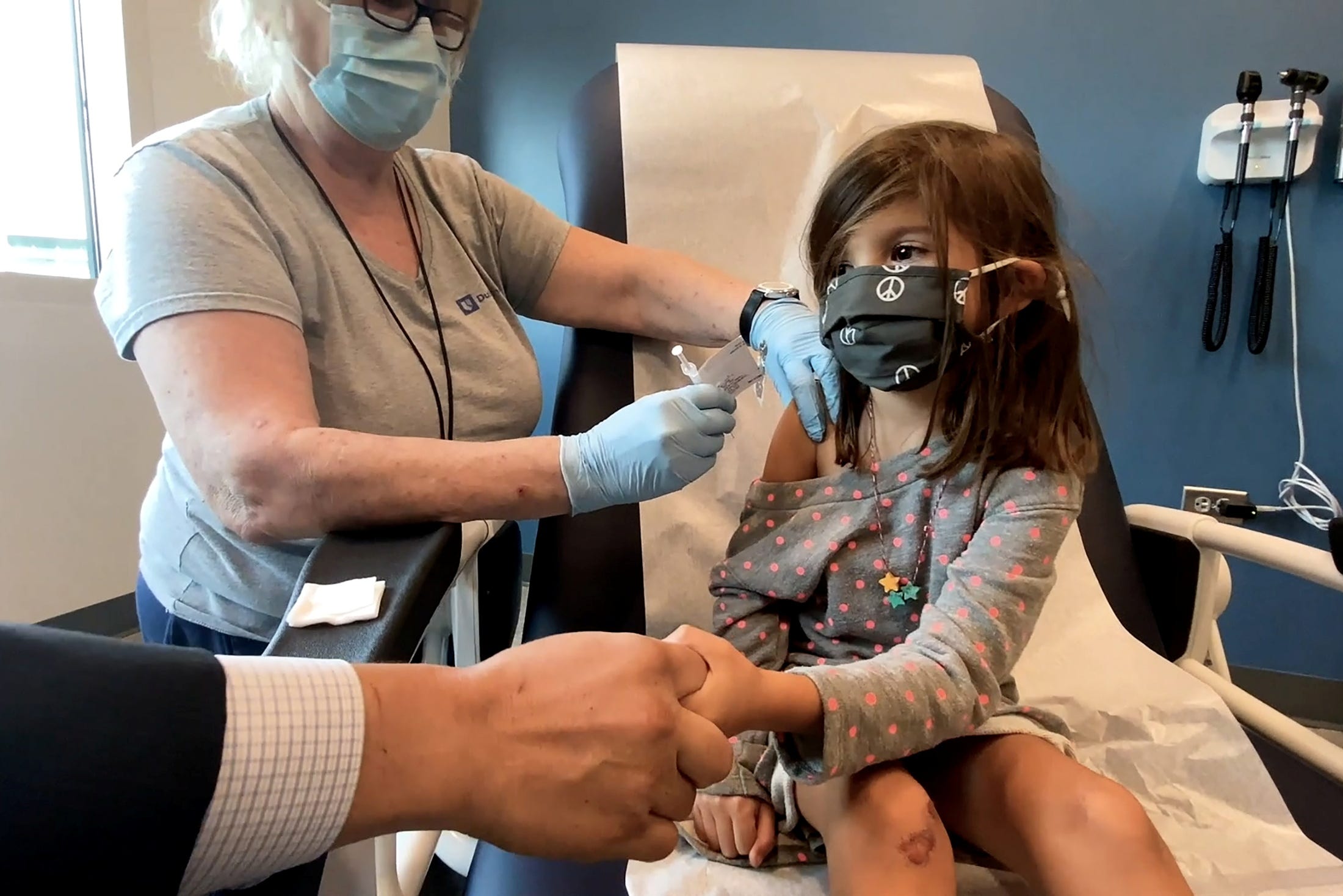 Bridgette Melo, 5, holds the hand of her father, Jim Melo, during her inoculation of one of two reduced 10 ug doses of the Pfizer BioNtech COVID-19 vaccine during a trial at Duke University in Durham, North Carolina September 28, 2021 in a still image from video. Video taken September 28, 2021.