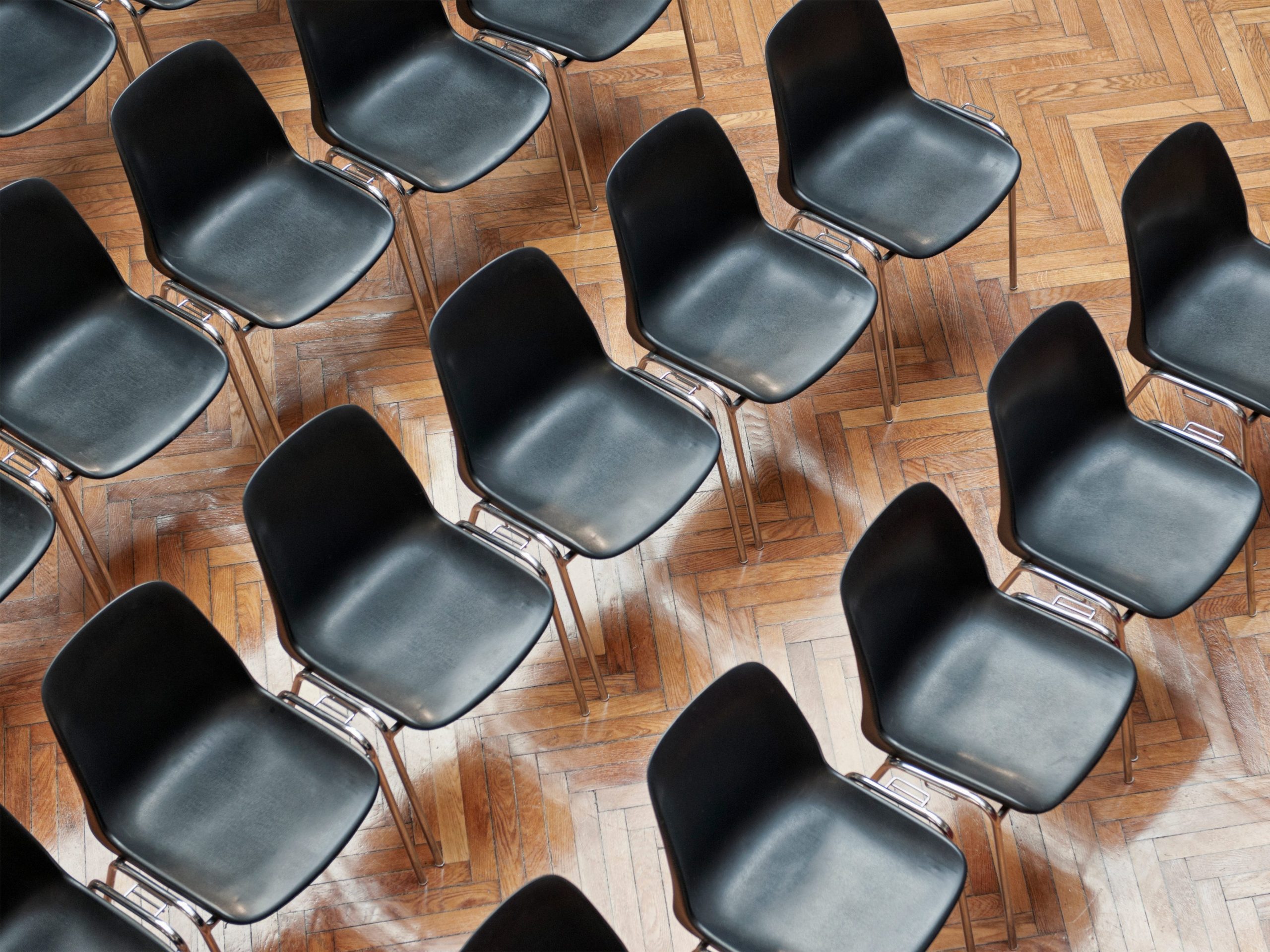 Rows of empty plastic chairs on a wooden floor.