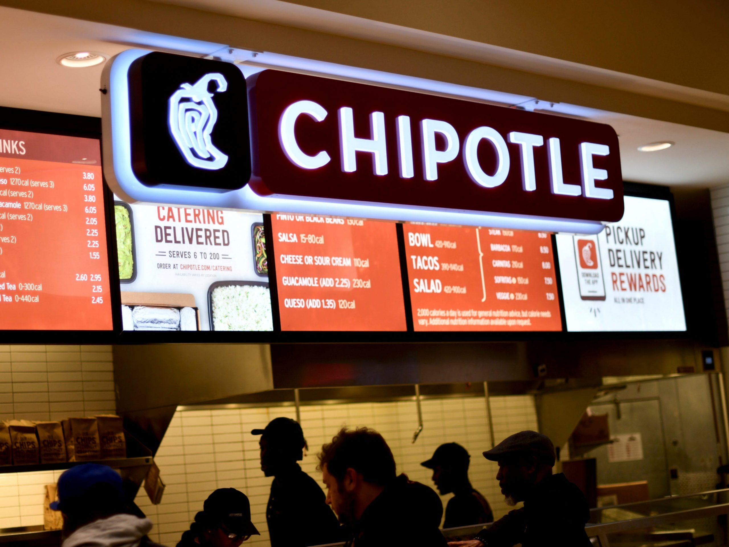 People crowd in front of a fast-food counter with a lighted Chipotle sign