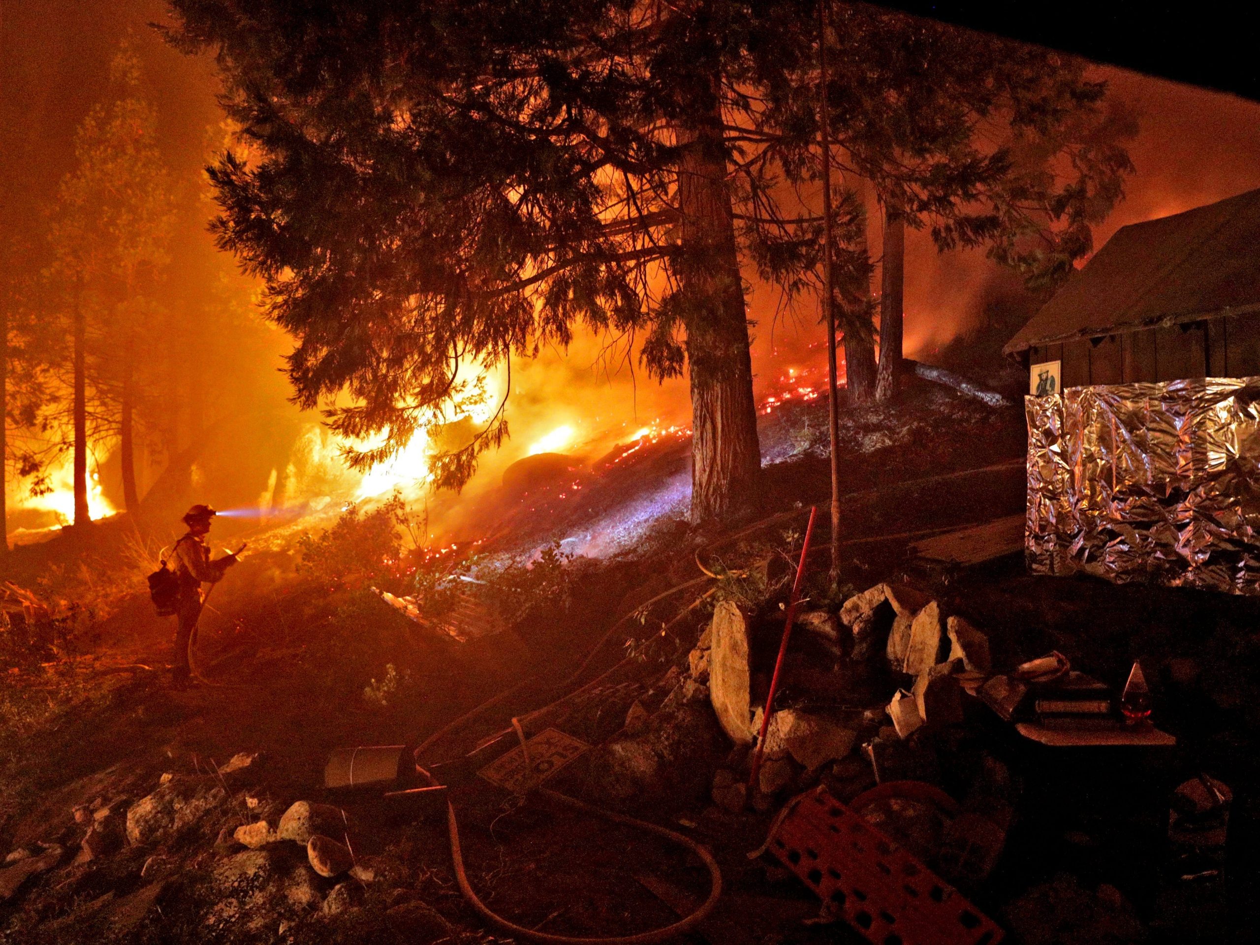 A firefighter next to a california wildfire near a cabin wrapped in foil