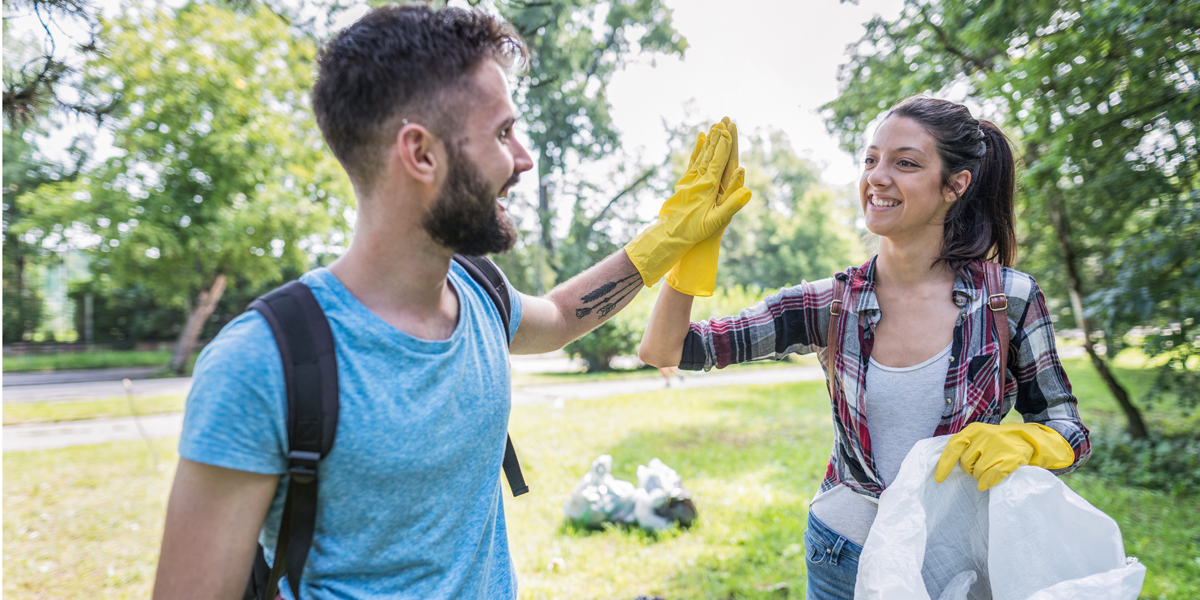 Two people smiling and high-fiving each other while picking up trash in a park.