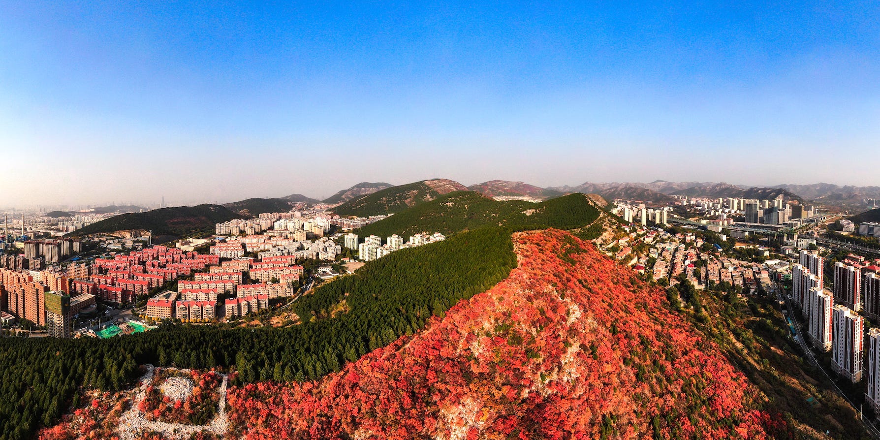 An aerial view of the Xiezi mountain shows the red-green mountain surrounded by city dwellings.