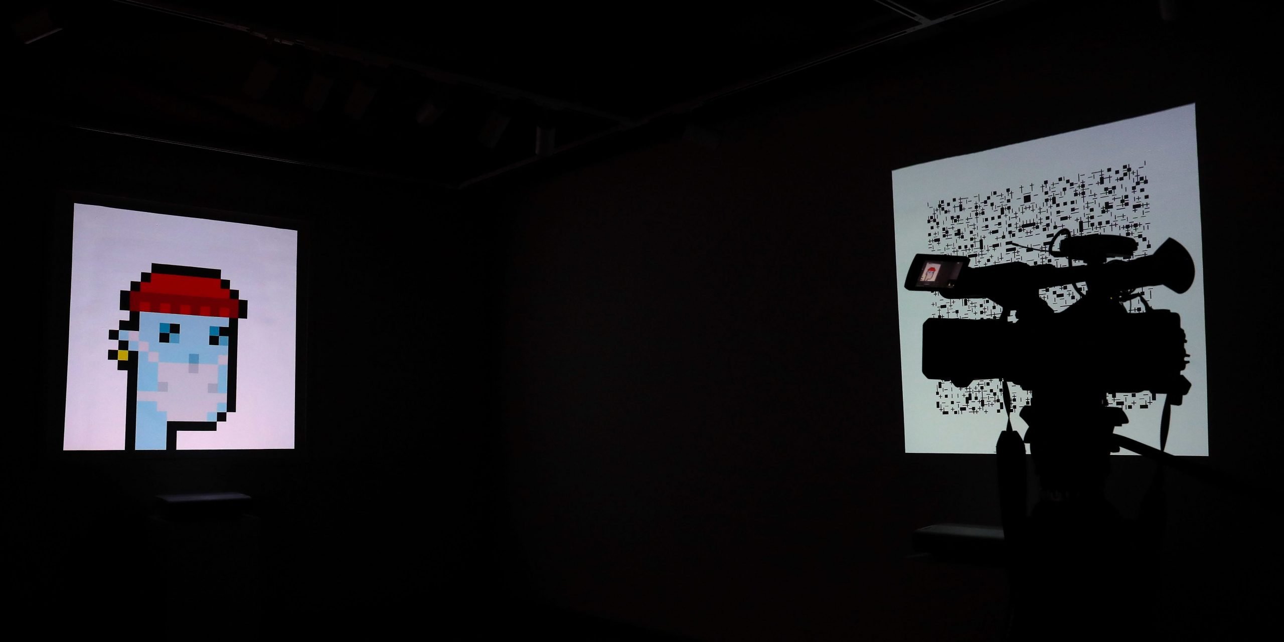 A television camera is seen in silhouette standing in front of "Autoglyph #177", a non-fungible token (NFT), and "CryptoPunk #7523", a series of 10,000 unique pixel-art characters made by Larva Labs in 2017, during a media preview for the "Natively Digital: A Curated NFT Sale" auction at Sotheby's in New York City, U.S., June 4, 2021.