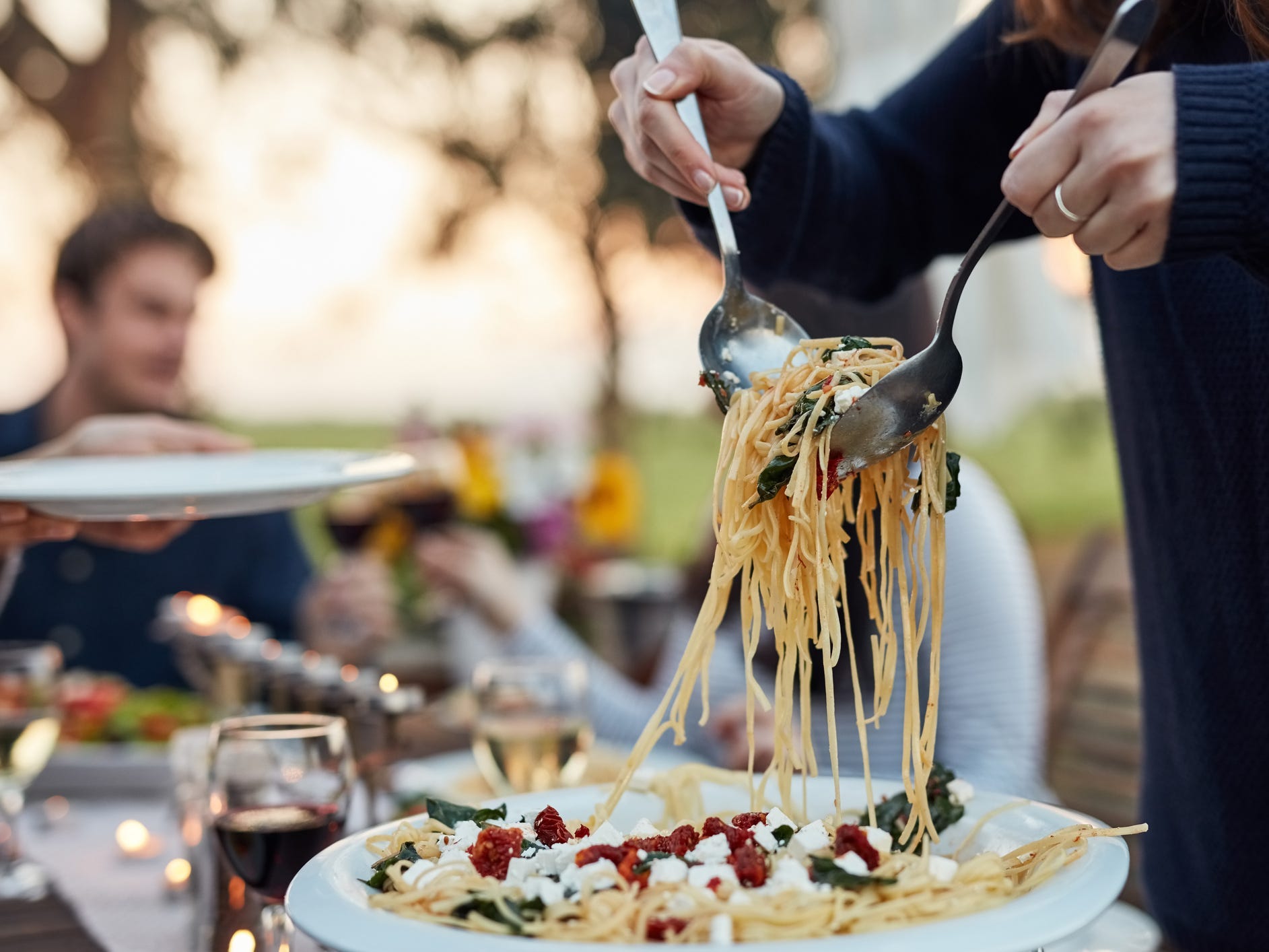 a closeup of a person's hands dishing up a large plate of pasta at a dinner event