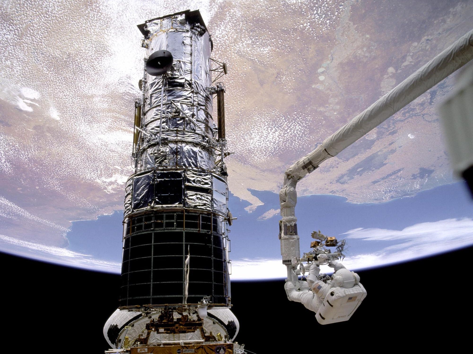 two astronauts in spacesuits work on the hubble space telescope in space above earth