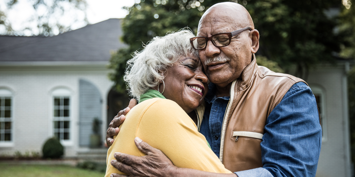 Senior couple embracing and smiling in front of a house.