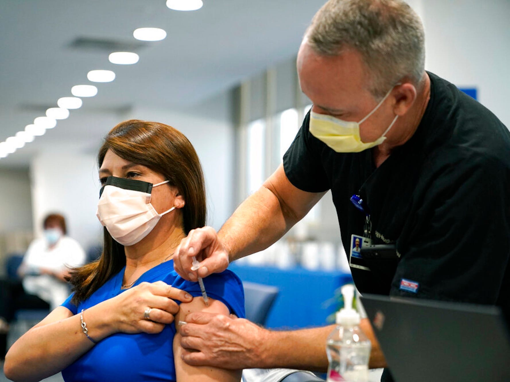 A woman wearing a mask and blue scrubs gets a shot in a clinic.