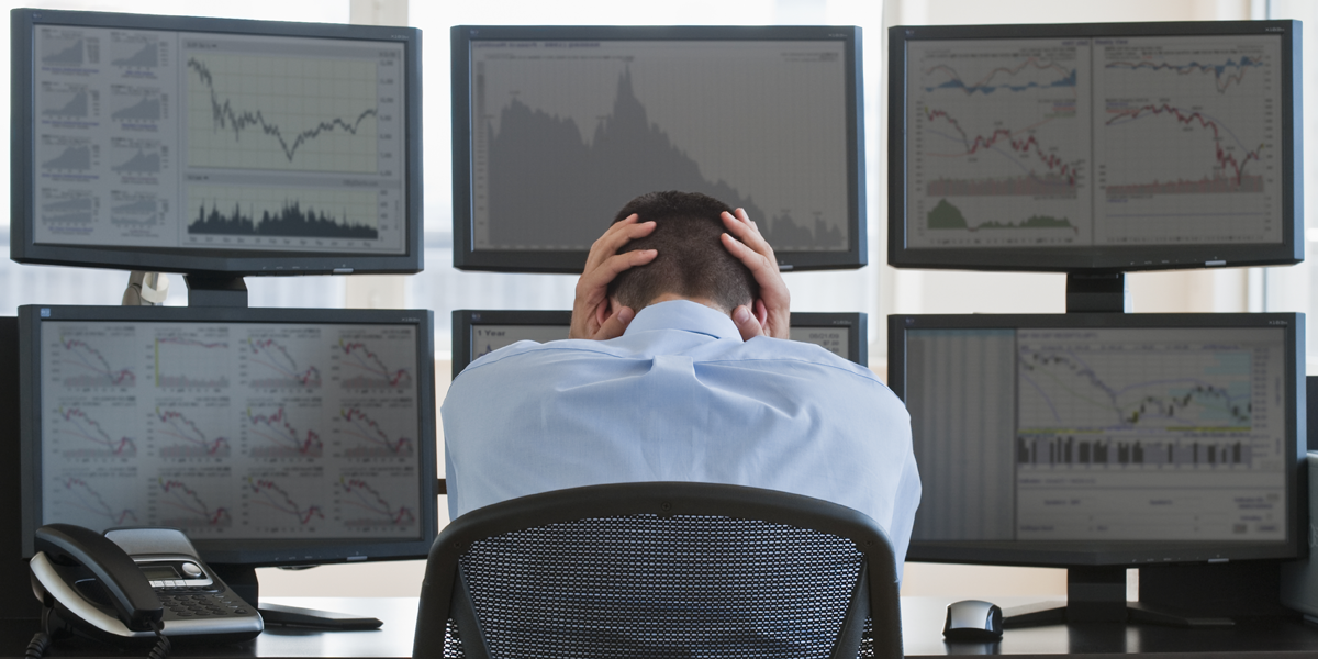 Frustrated stock trader gripping his head while sitting at his computer.