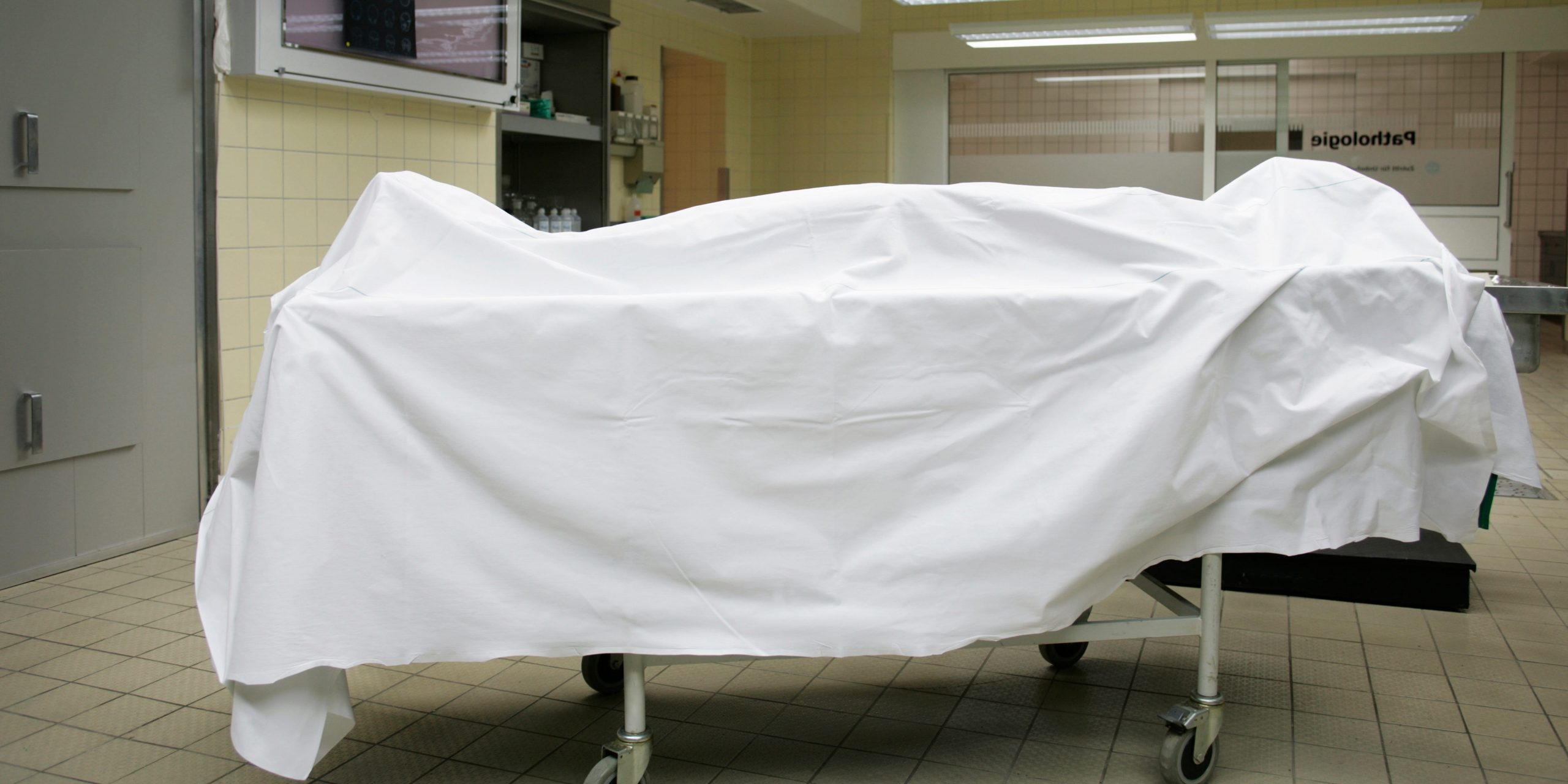 A body covered in a sheet in a hospital room.