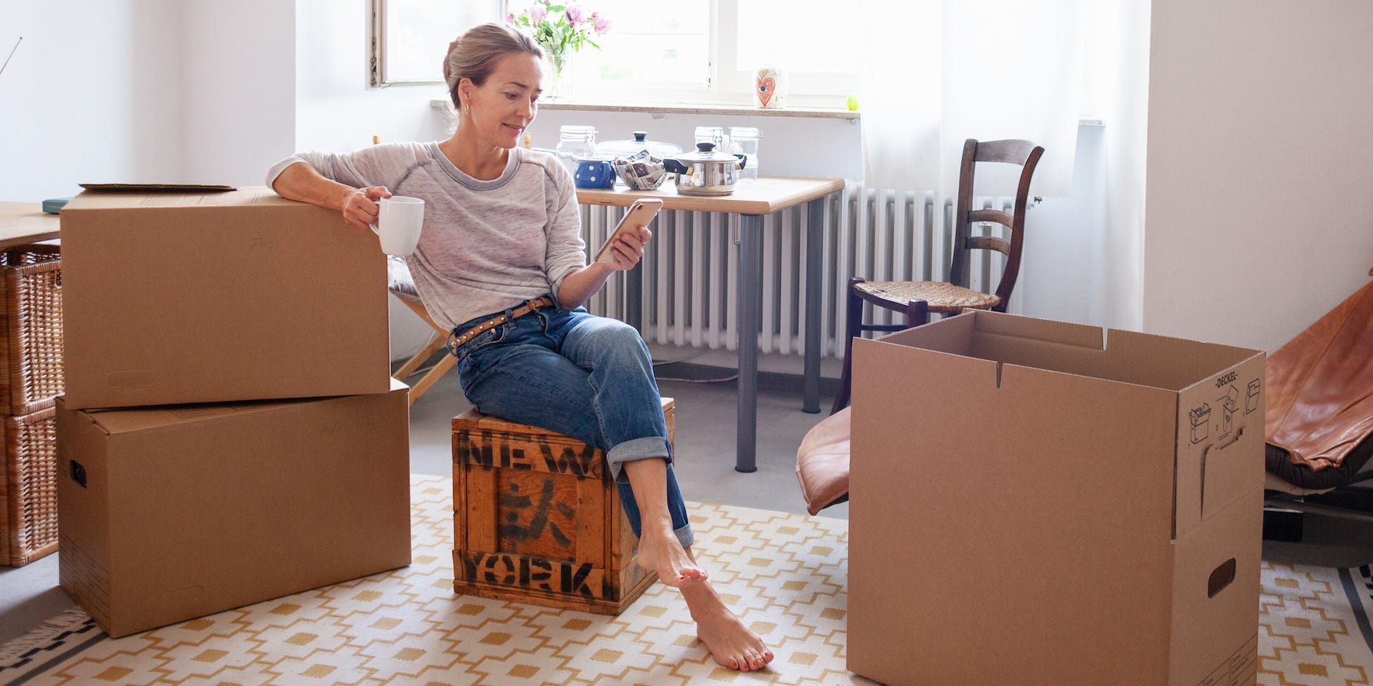 woman packing up apartment with boxes around her, holding smartphone