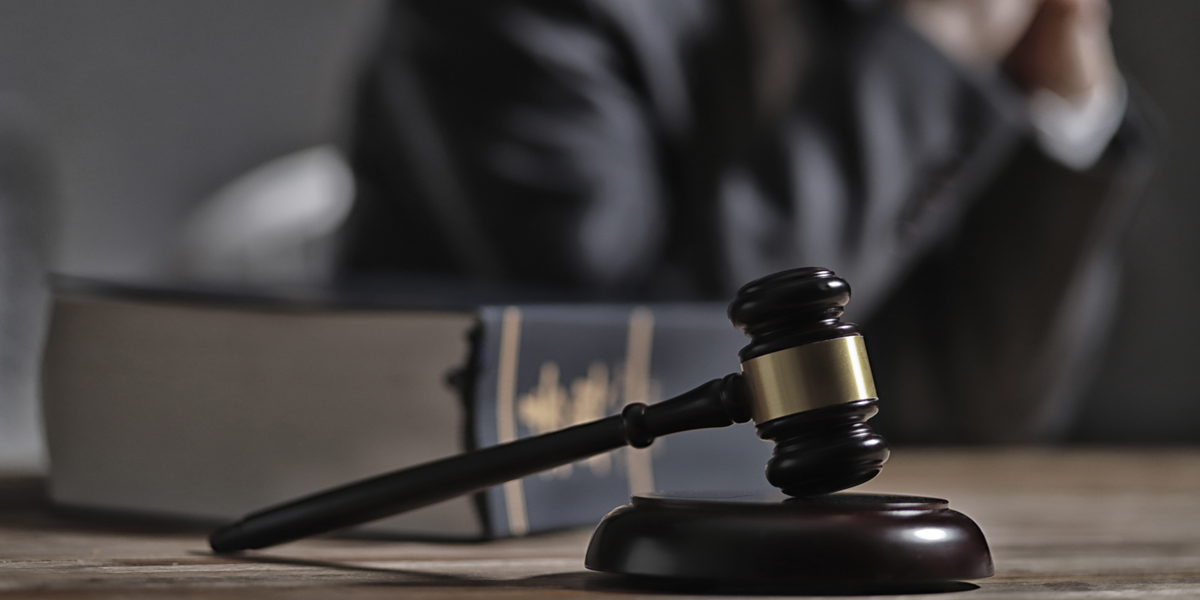 A photo of a gavel with a law book and judge in the background.