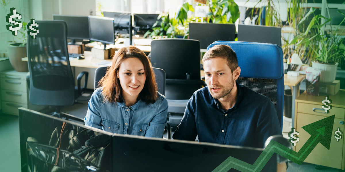 Two colleagues sitting next to each other and looking at a dual monitor at work.