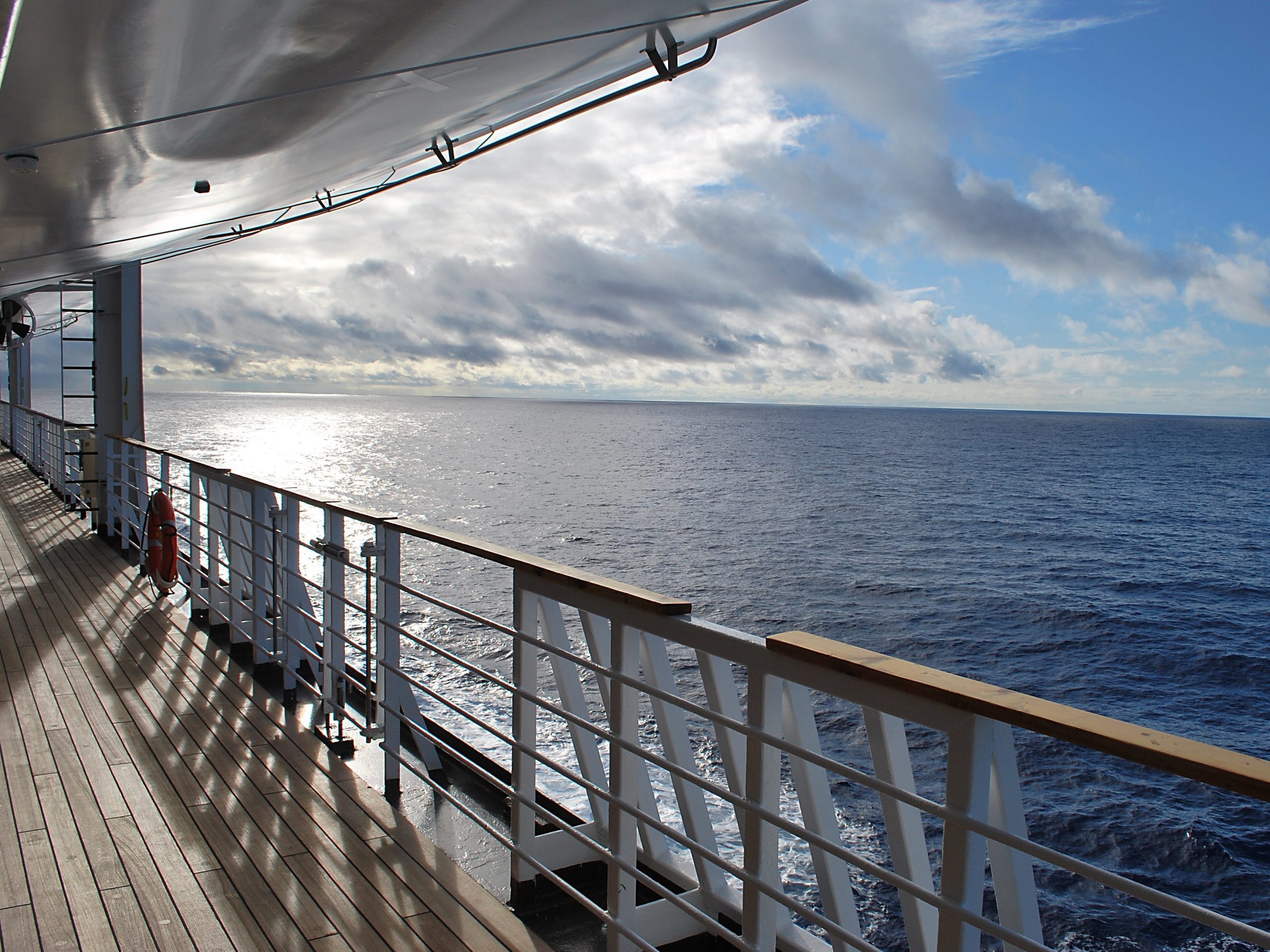 A view of the side of a cruise ship - railing and a flat blue ocean