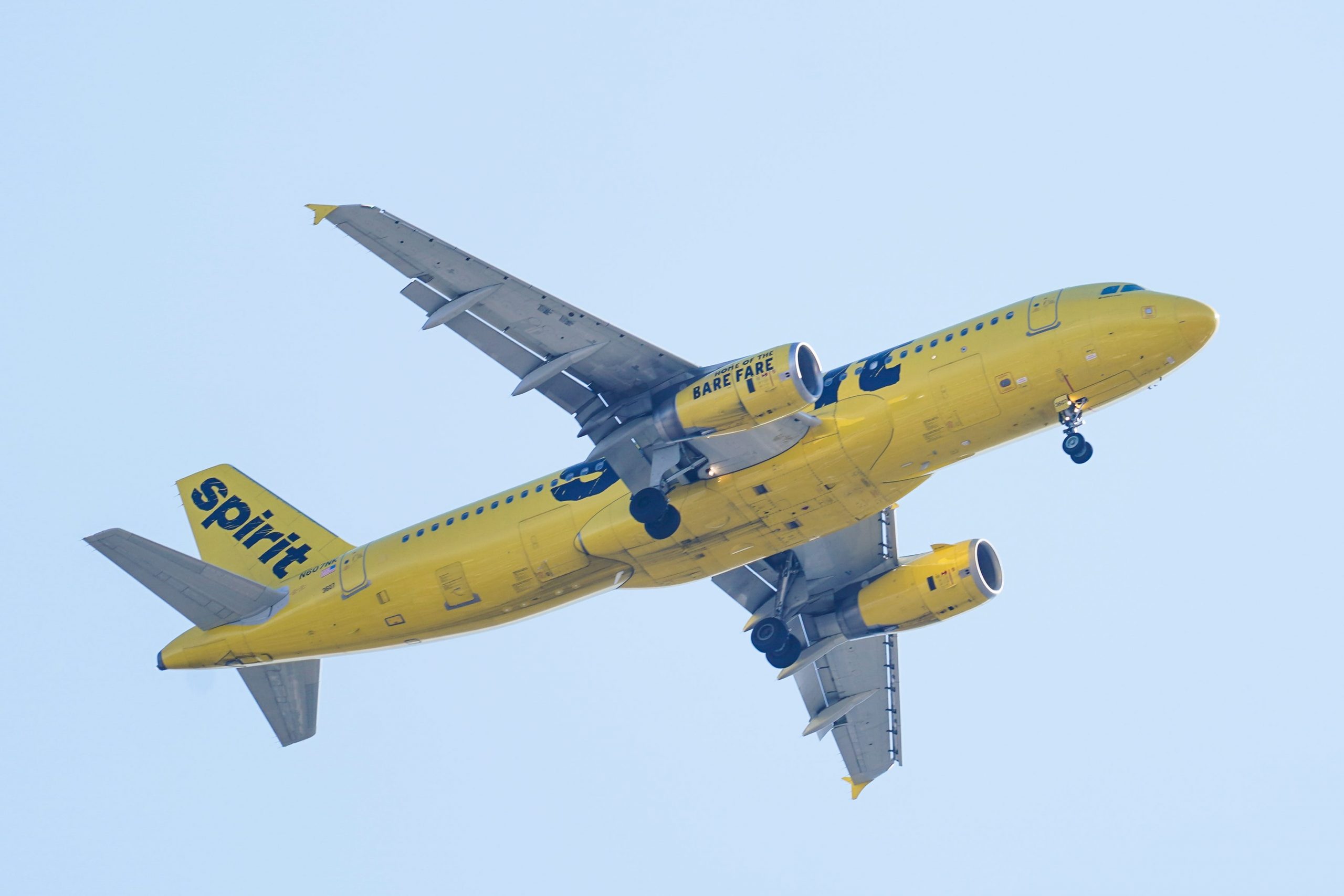 A yellow Spirit Airlines plane descending against a pale blue sky