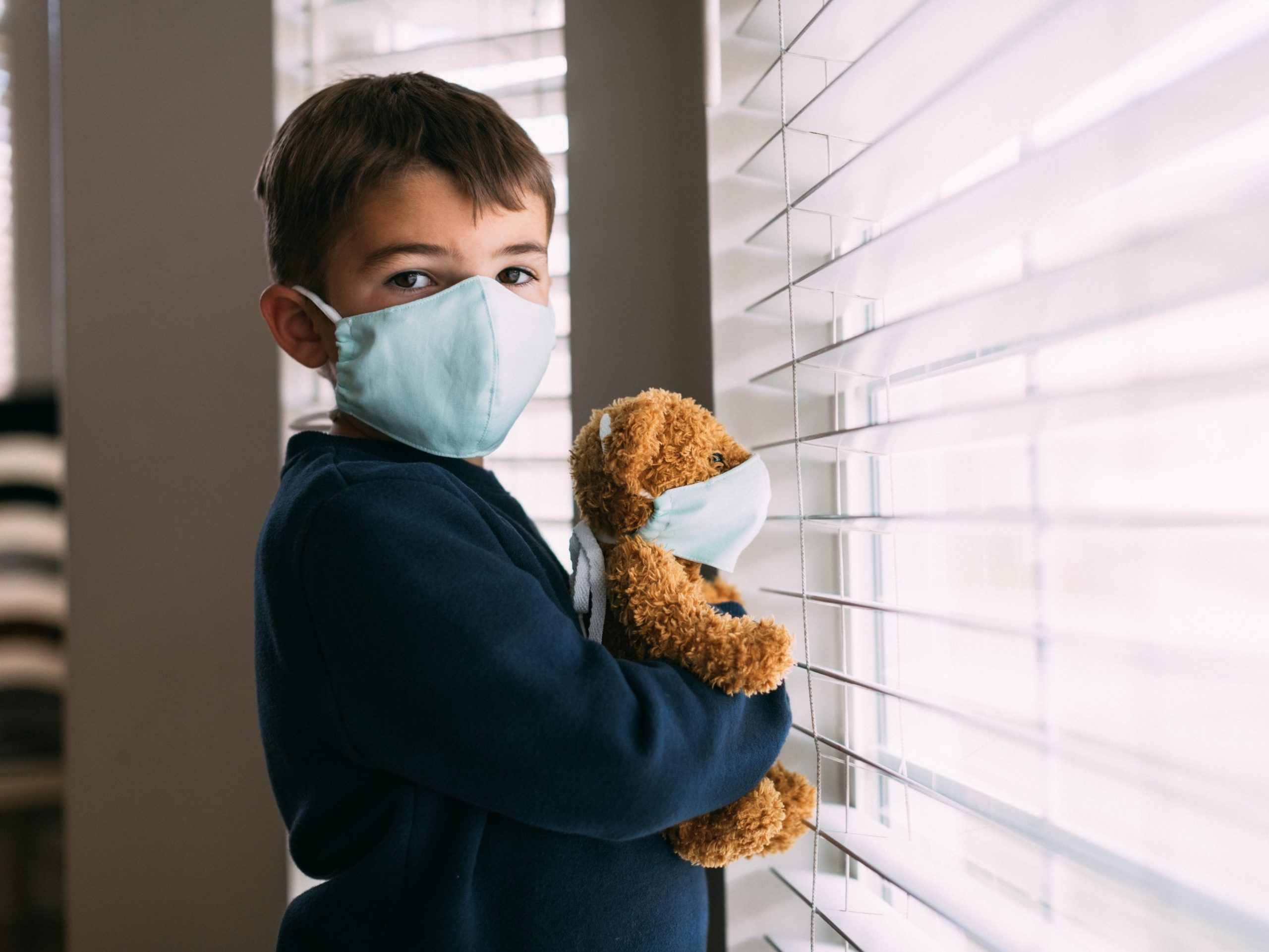 Child wearing a mask looking out the window